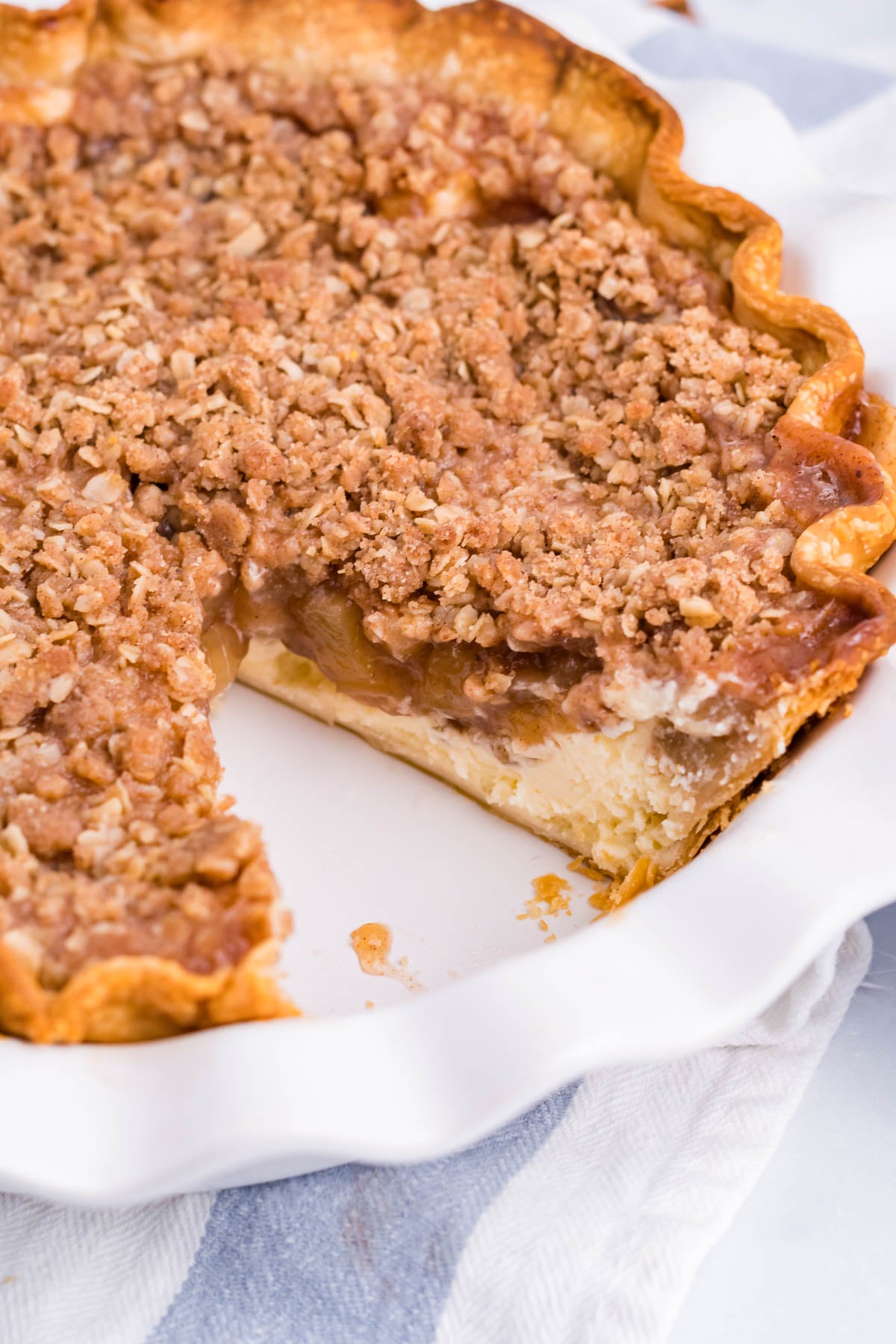 Close up view of Apple Crumb Cheesecake Pie in a white pie dish with a slice removed.