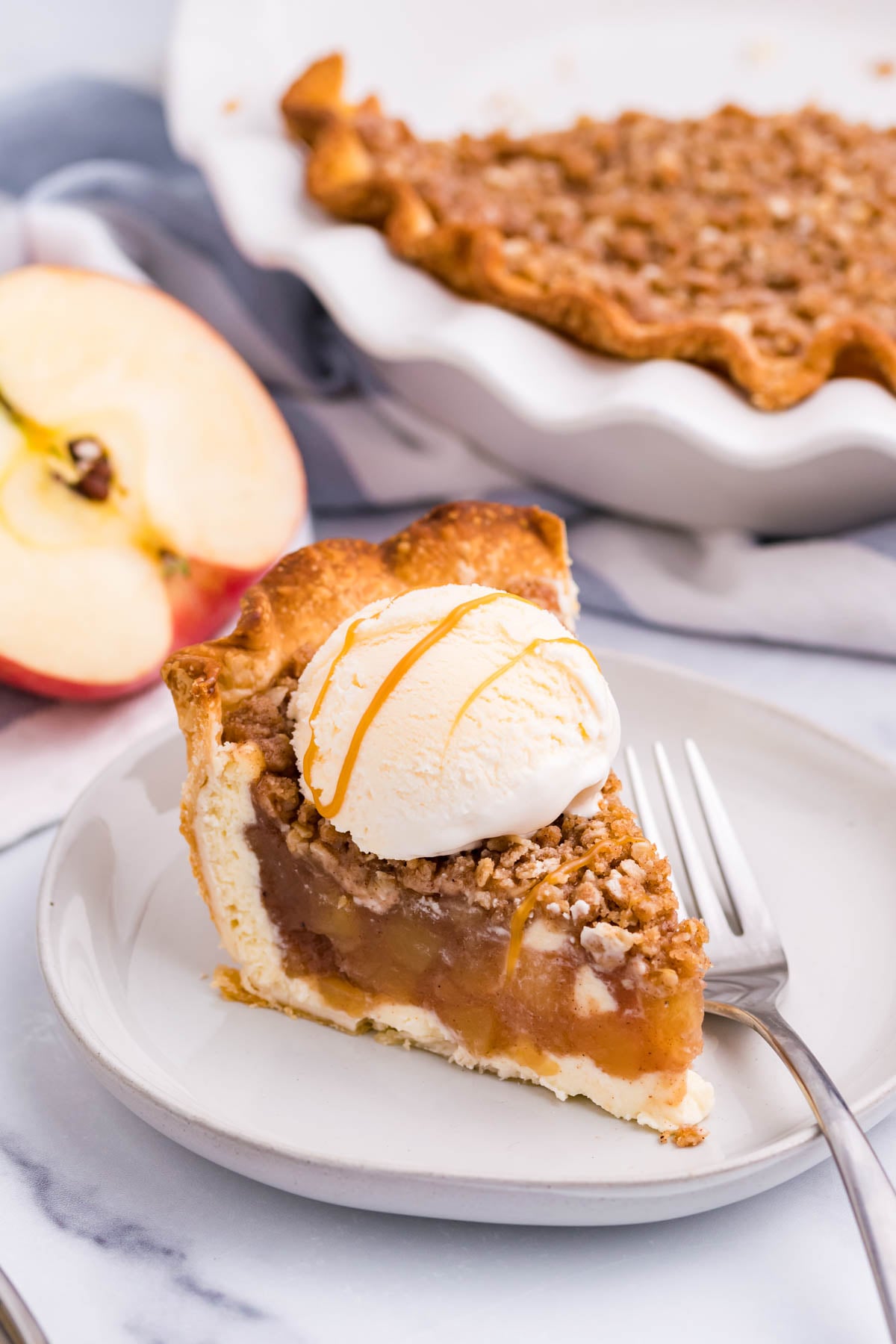 Front view of a slice of Apple Crumb Cheesecake Pie on a white dish with a scoop of vanilla ice cream.