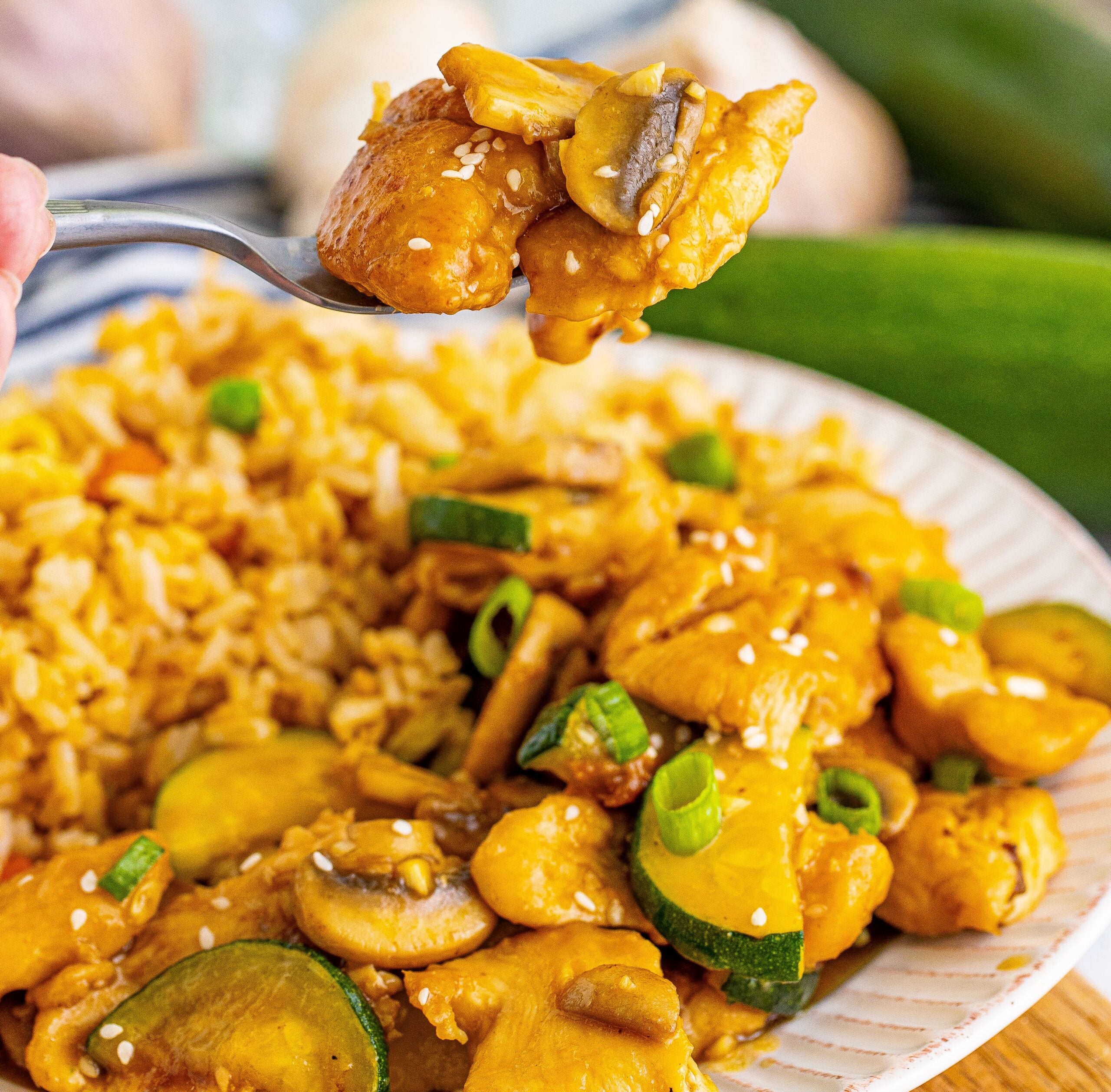 Front view of Panda Express Mushroom Chicken on a white dish served with fried rice with a spoon lifting up a bite