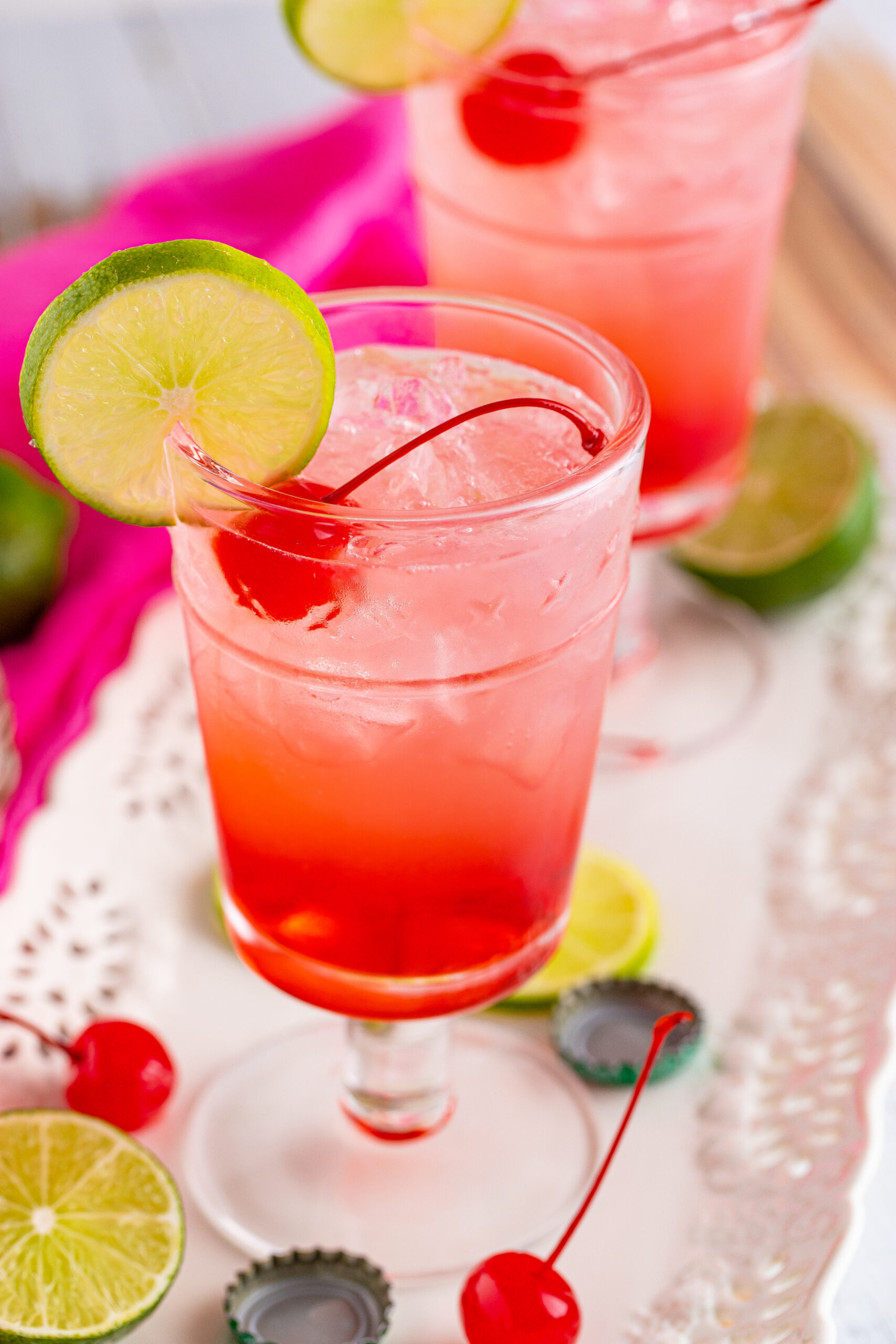 Side view of Dirty Shirley Temple garnished with a lime slice and cherry.