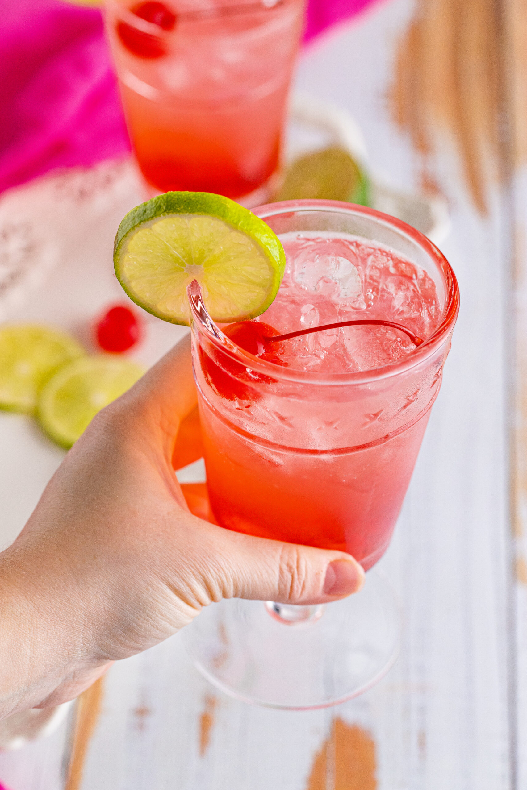 45 degree view of Dirty Shirley Temple garnished with a lime slice being held.