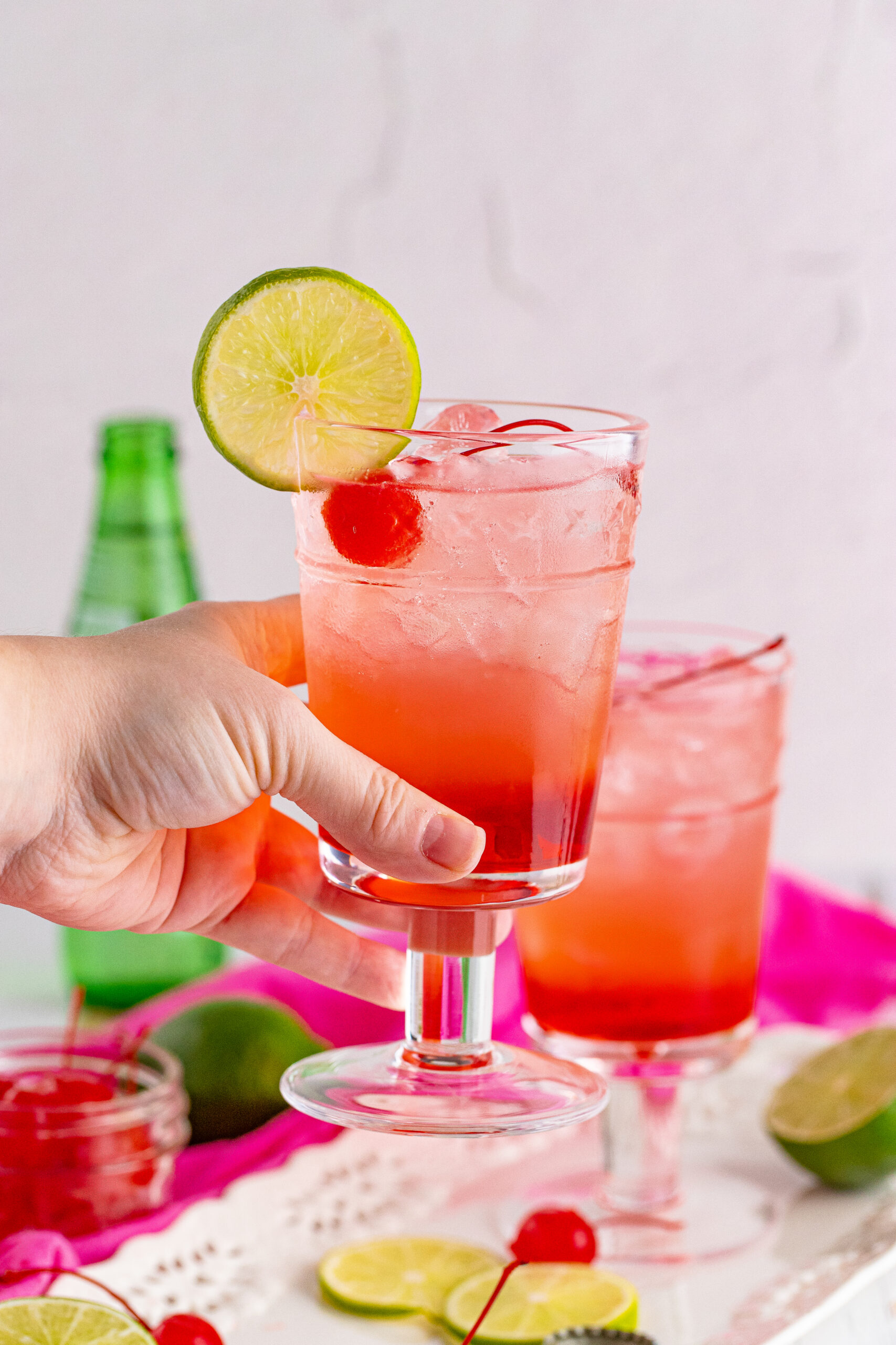 Side view of Dirty Shirley Temple garnished with a lime slice being held.