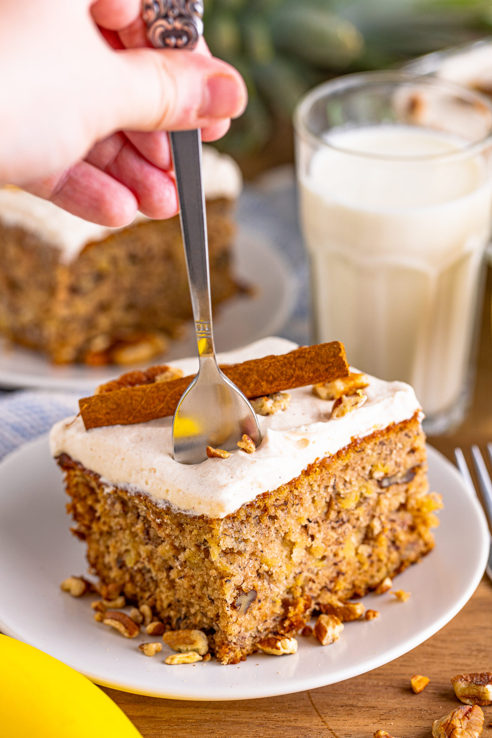 Front view of Hummingbird Cake on a white dish garnished cinnamon stick with a silver fork removing a bite.