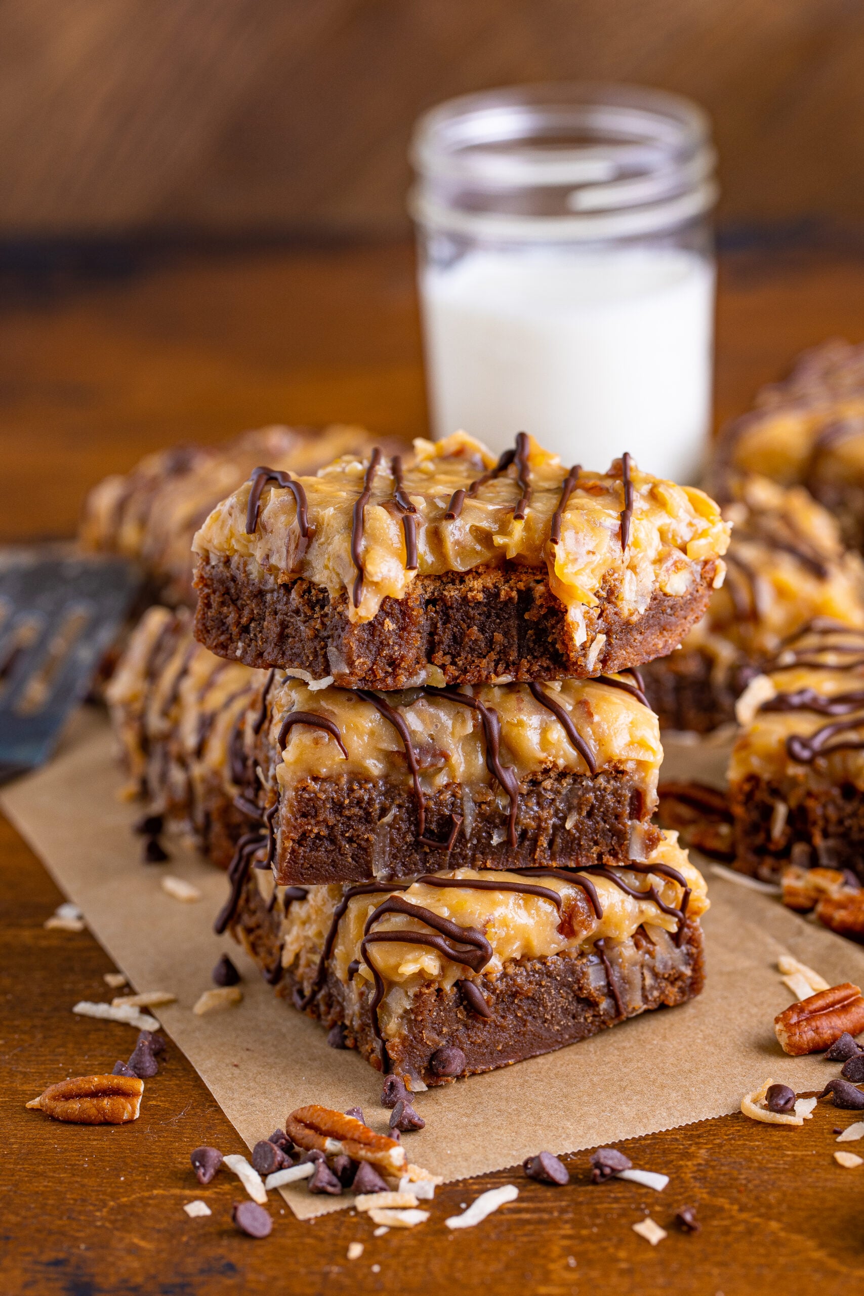 Front view of three German Chocolate Brownies stacked on a piece of parchment paper with a bite removed from the top German Chocolate Brownie.