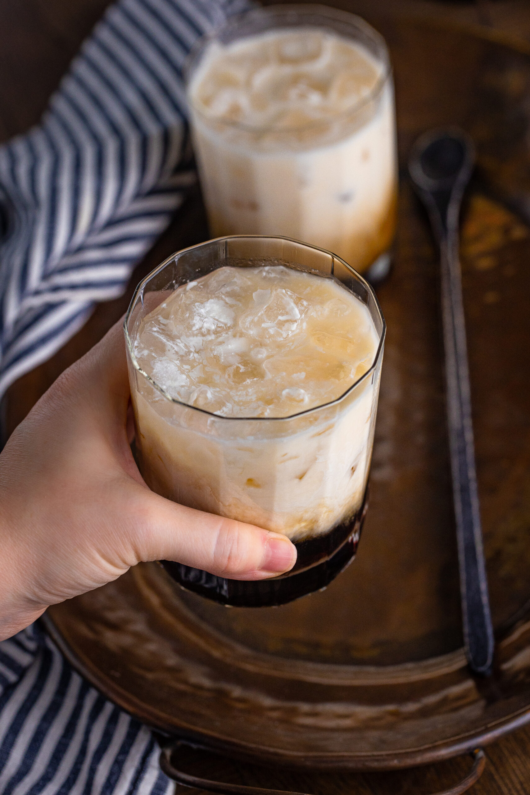 A hand holding a White Russian drink in a clear glass.