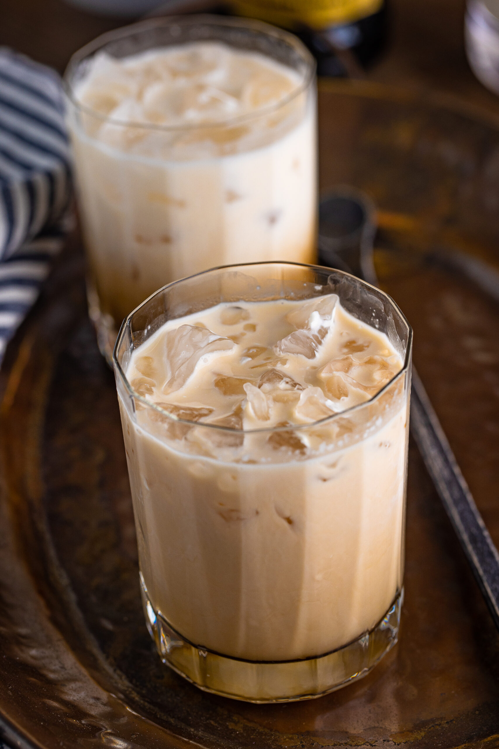 White Russian mixed up on a clear glass sitting on a dark metal serving tray.