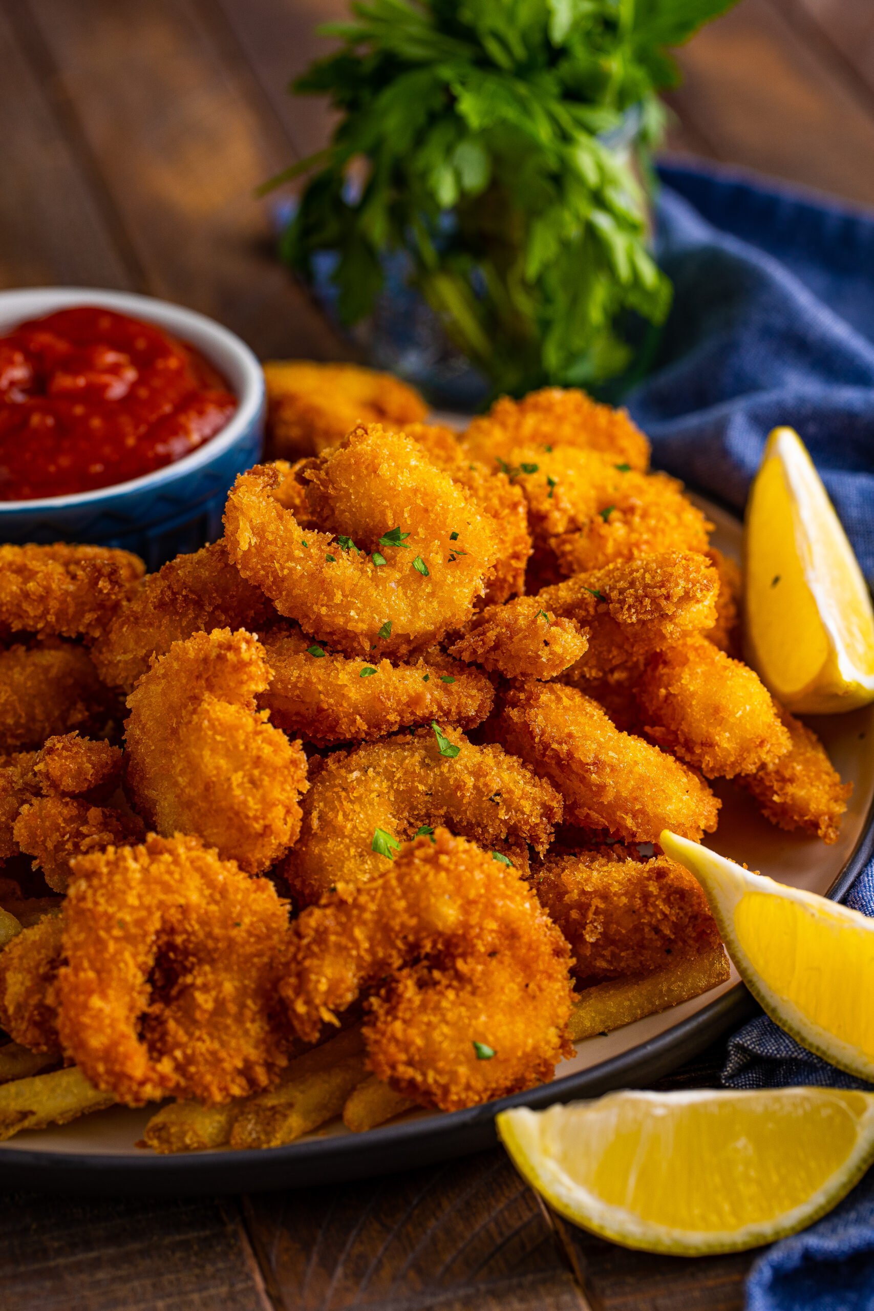 Front view of Panko Fried Shrimp on a dish served with french fries, cocktail sauce and lemon wedges.