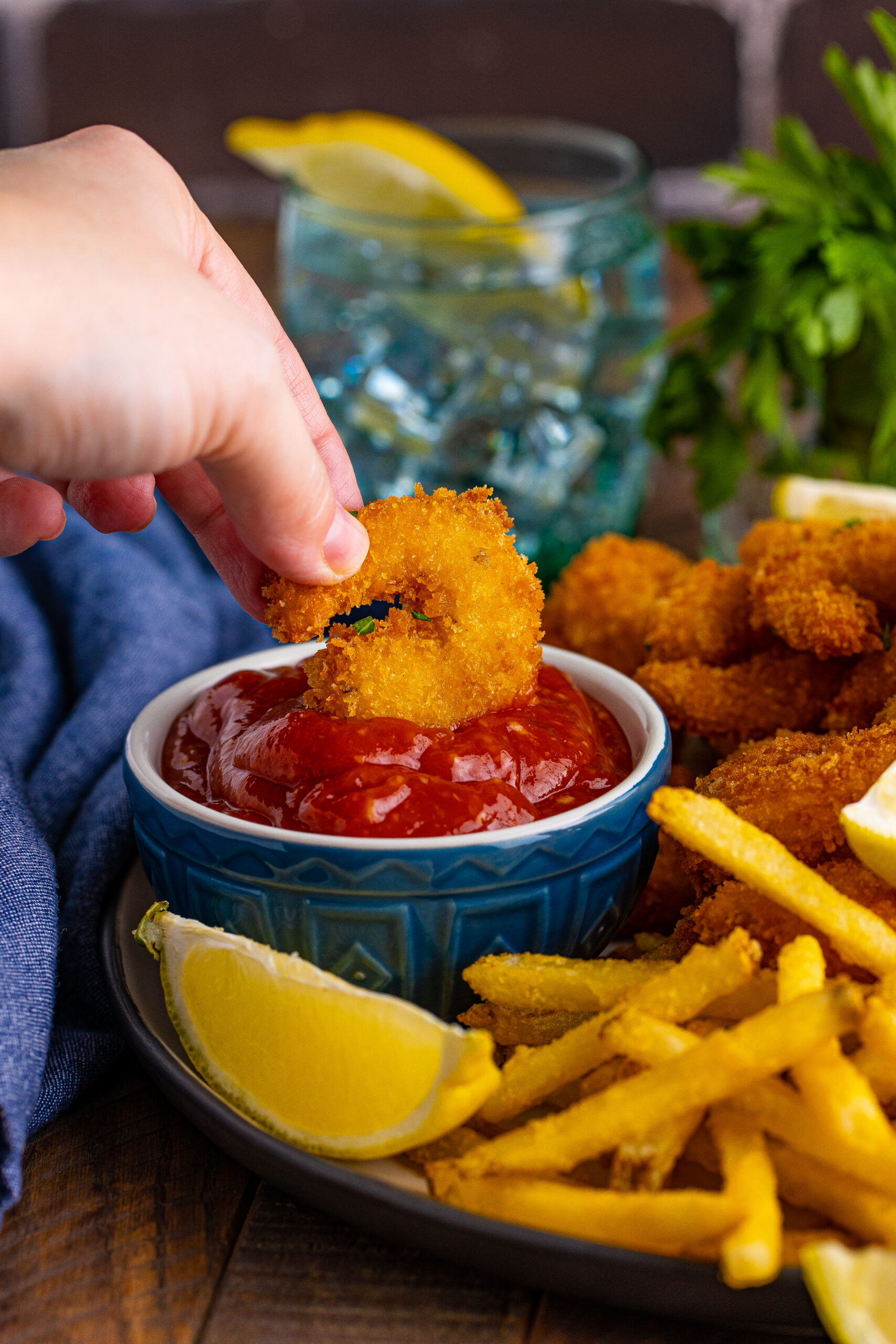 Front view of Panko Fried Shrimp being dipped into a blue bowl filled with cocktail sauce.