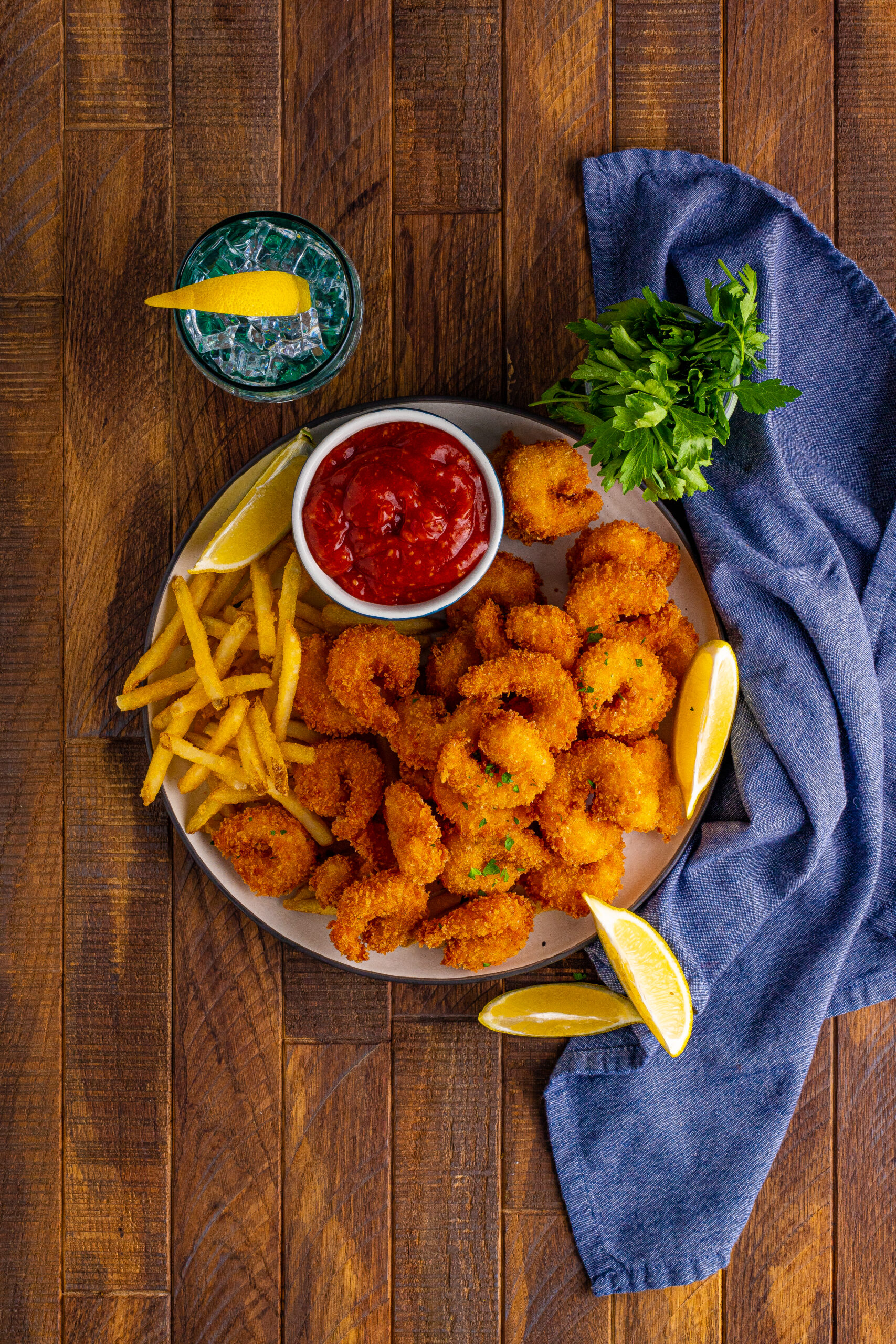 Overhead view of Panko Fried Shrimp on a dish served with french fries, cocktail sauce and lemon wedges.