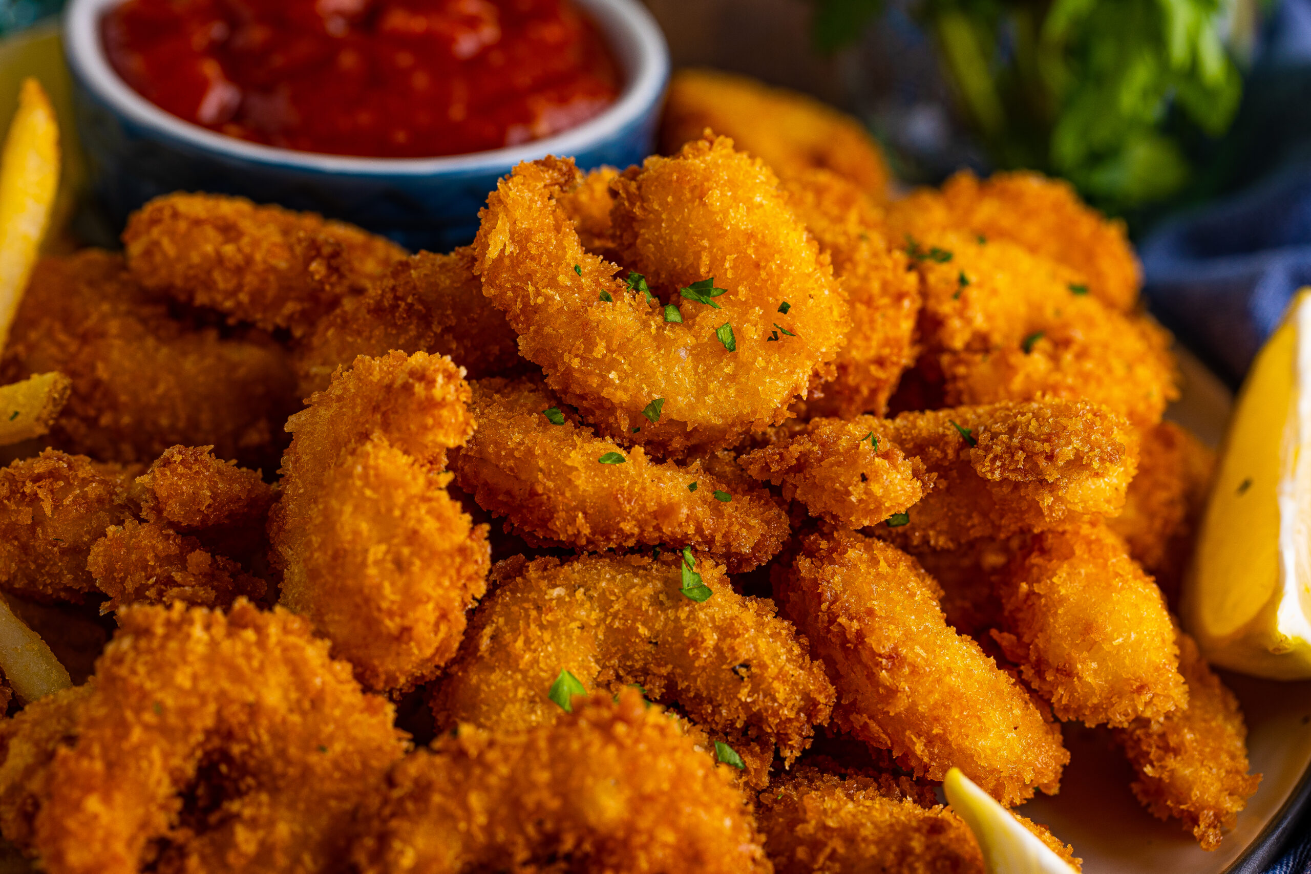 Front view of Panko Fried Shrimp on a dish served with cocktail sauce and lemon wedges.