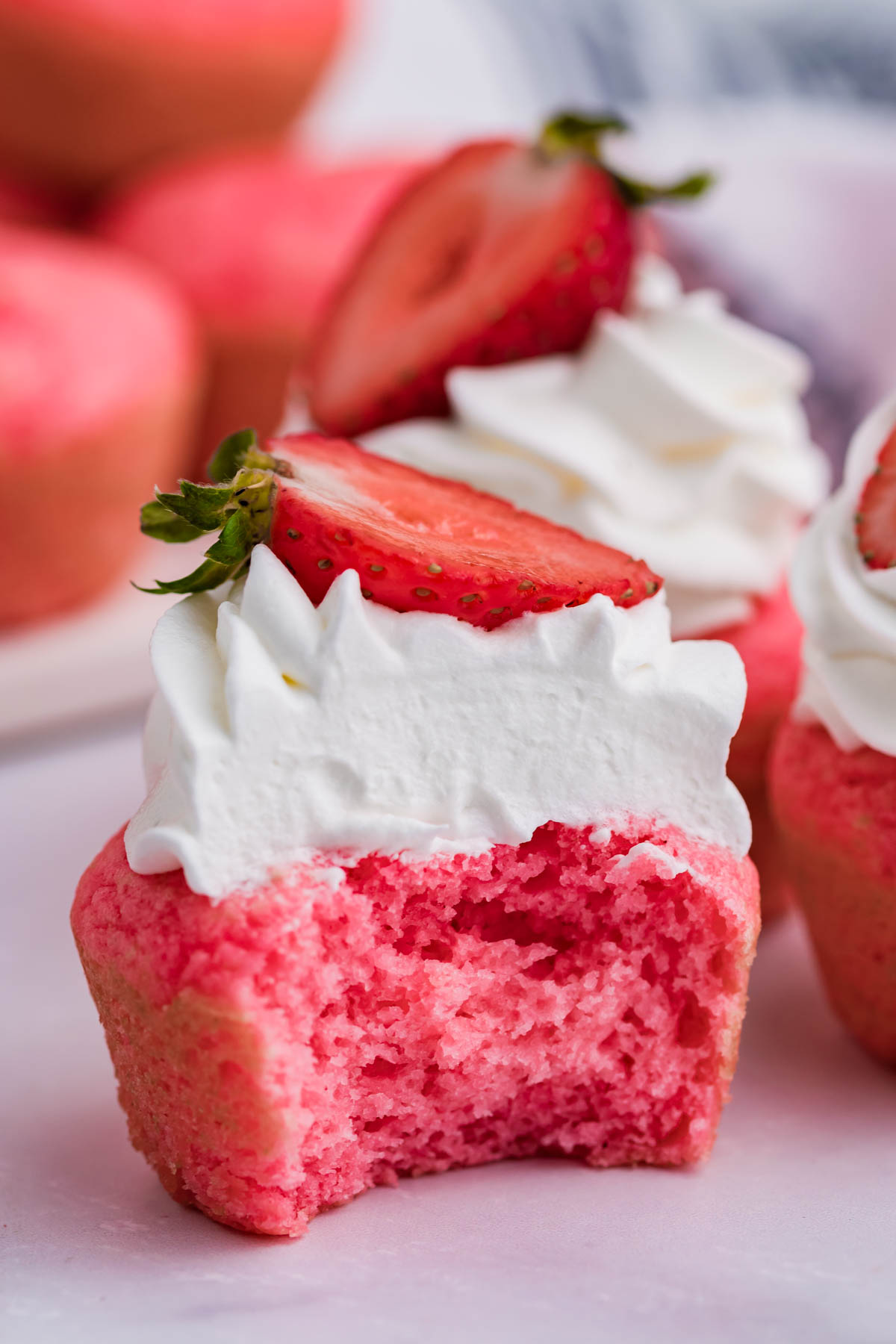 Front view of a Weight Watchers Strawberry Muffin topped with whipped cream and strawberry half with a bite removed.