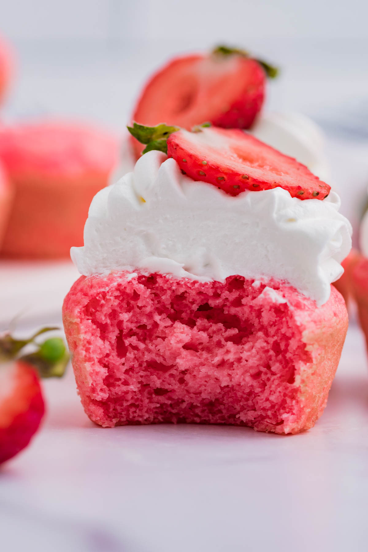 Front view of a Weight Watchers Strawberry Muffin topped with whipped cream and strawberry half with a bite removed.