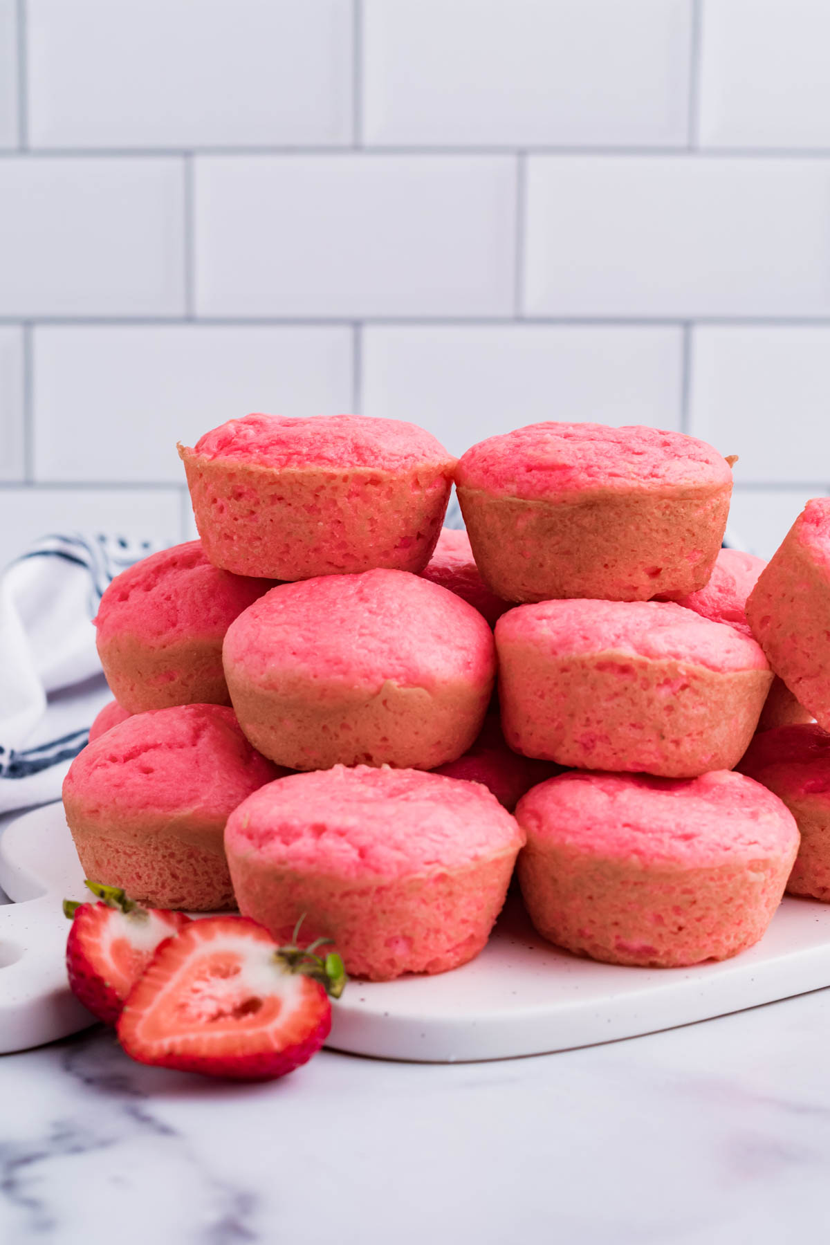 Front view of a stack of Weight Watchers Strawberry Muffins on a white cutting board.