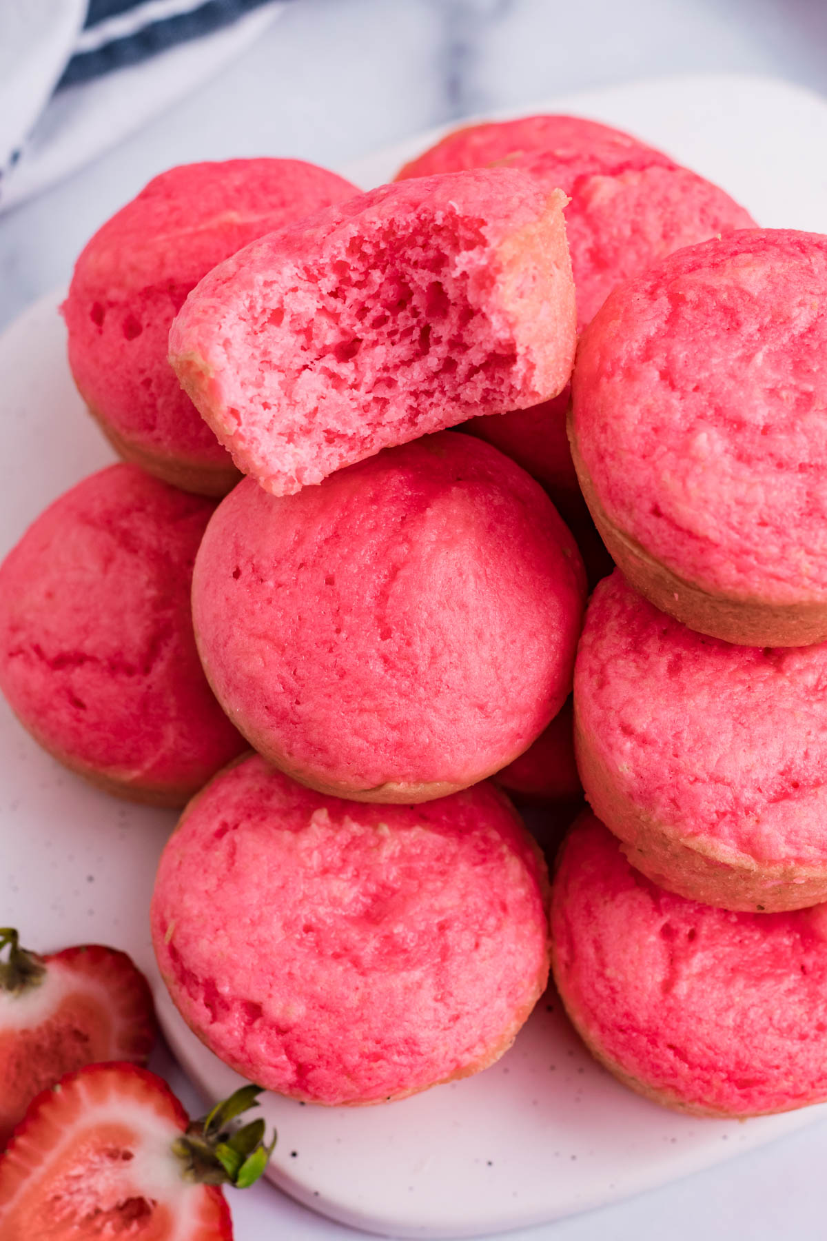 Overhead view of a stack of Weight Watchers Strawberry Muffins on a white cutting board with a bite removed from the top muffin.