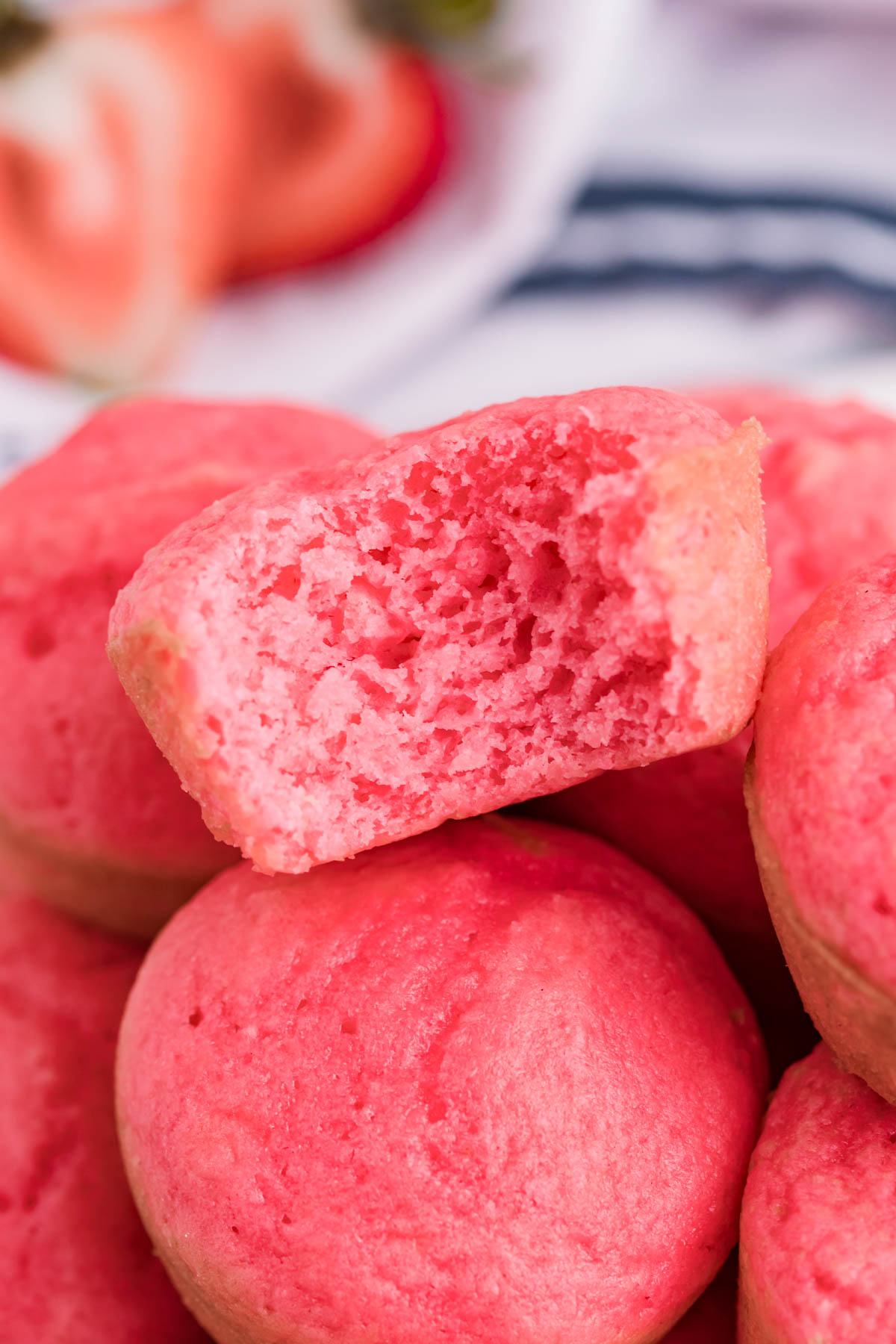 Close up view of a stack of Weight Watchers Strawberry Muffins on a white cutting board with a bite removed from the top muffin.