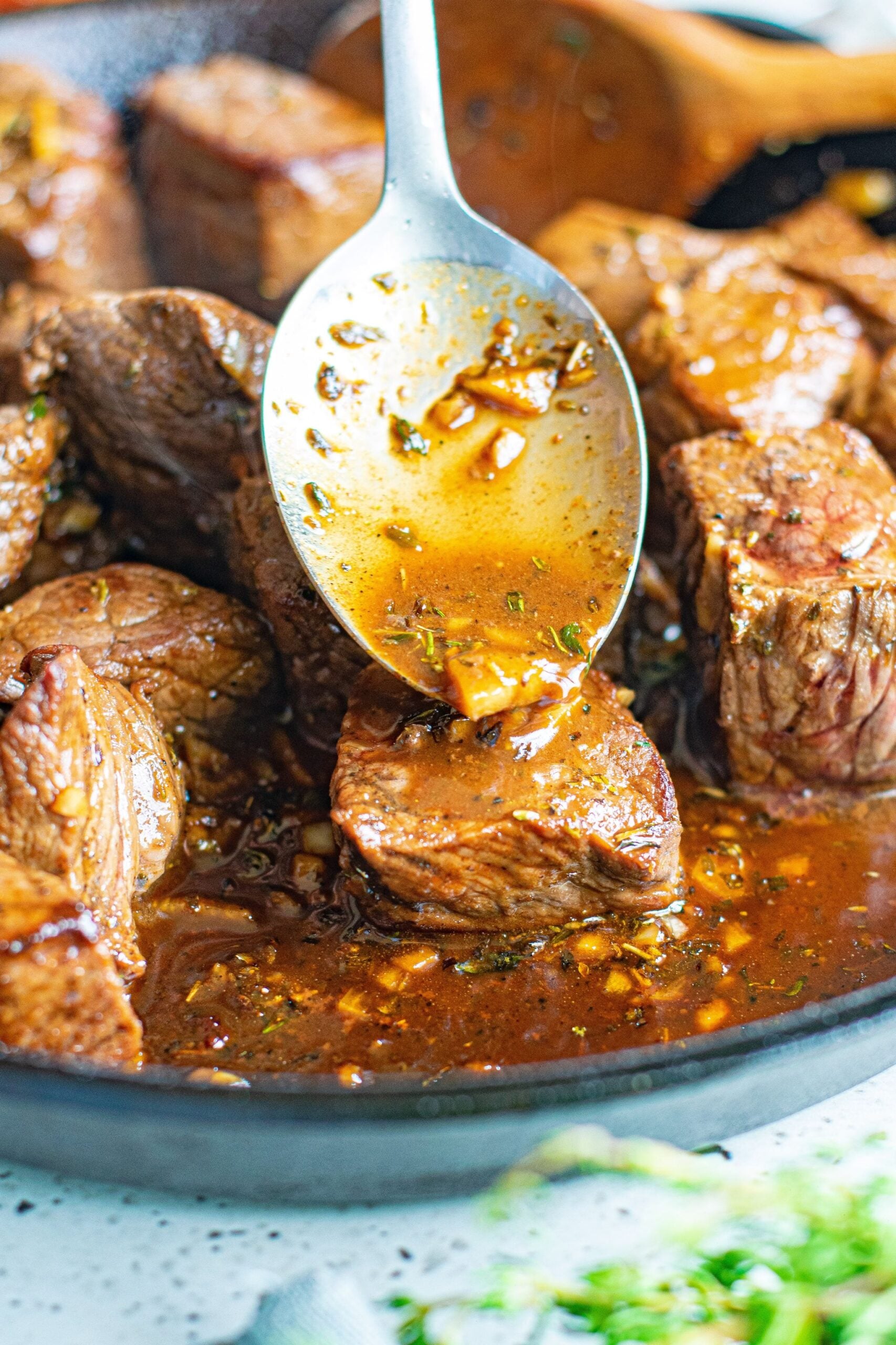 Close up view of a silver spoon spooning the garlic honey sauce on to the Garlic Honey Steak Bites.