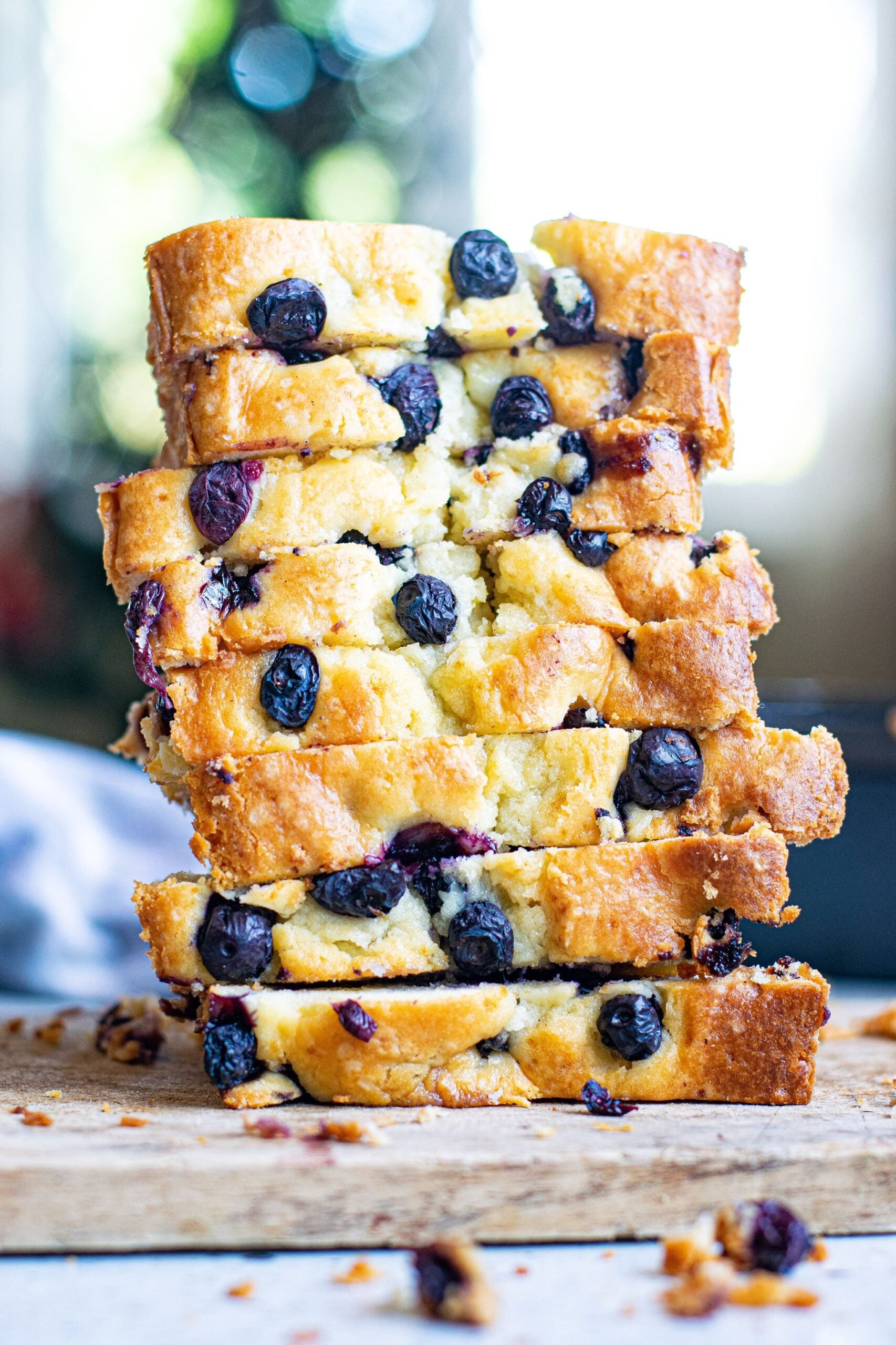 Side shot of eight slices of blueberry cream cheese loaf stacked on top of each other on a wooden board.