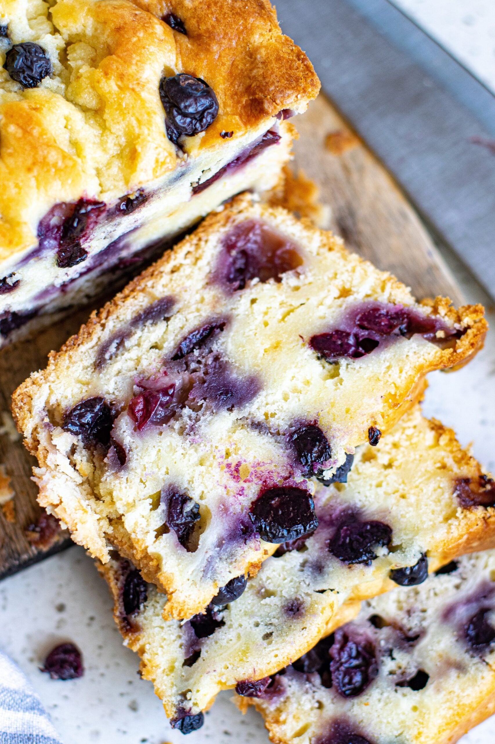 Three slices of blueberry cream cheese loaf stacked on a wood serving tray.