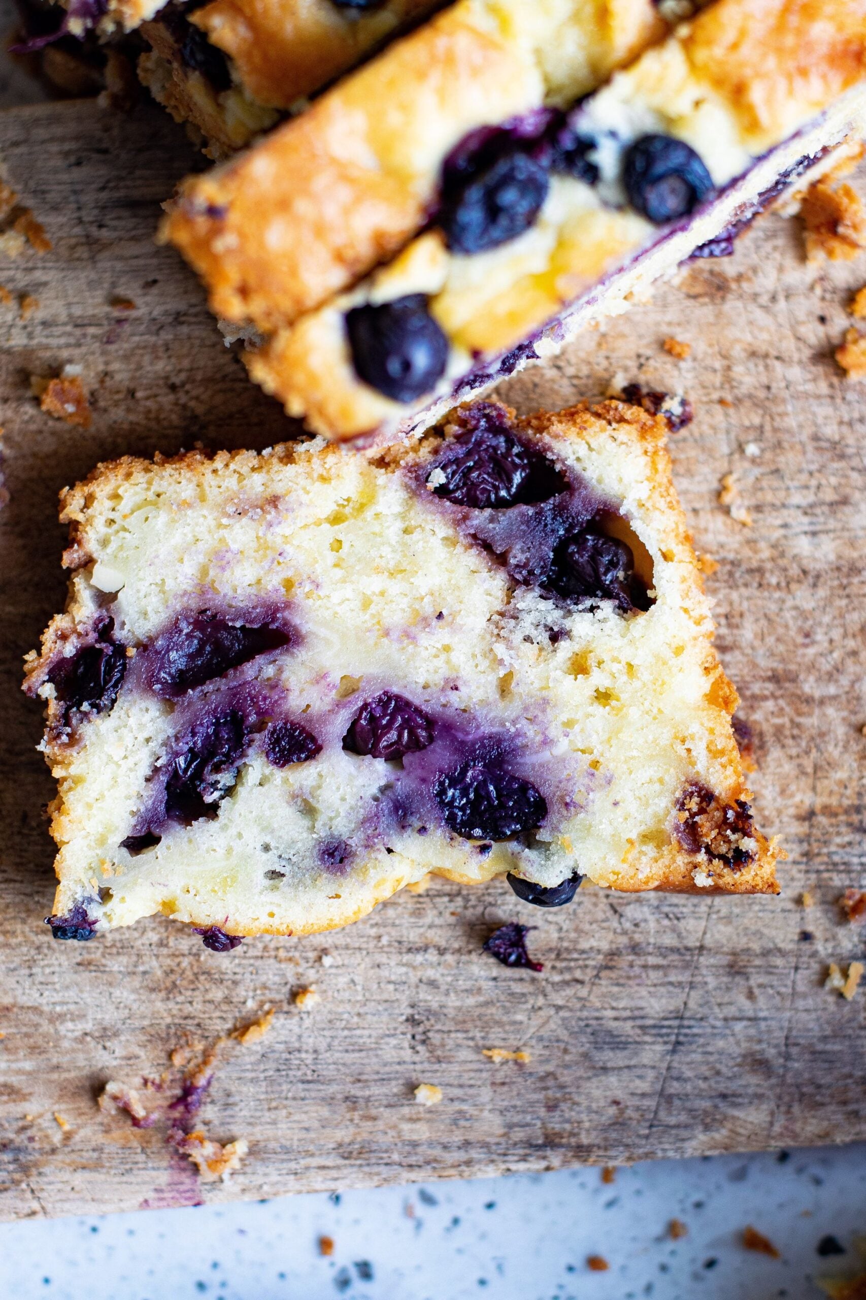 Overhead shot of a slice of blueberry cream cheese loaf on a wooden cutting board.