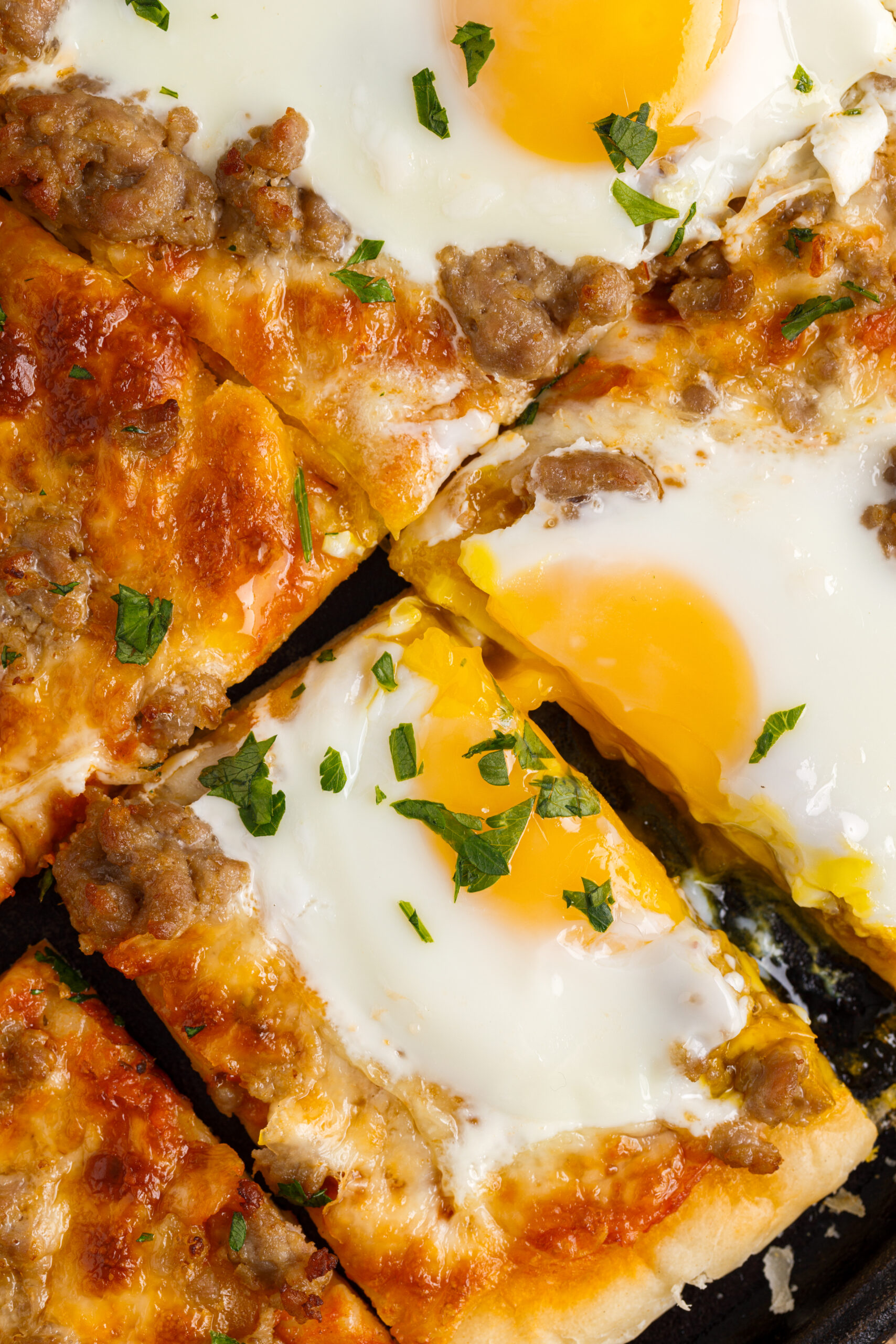 Close up view of Breakfast Pizza on a black pizza dish cut into square slices.