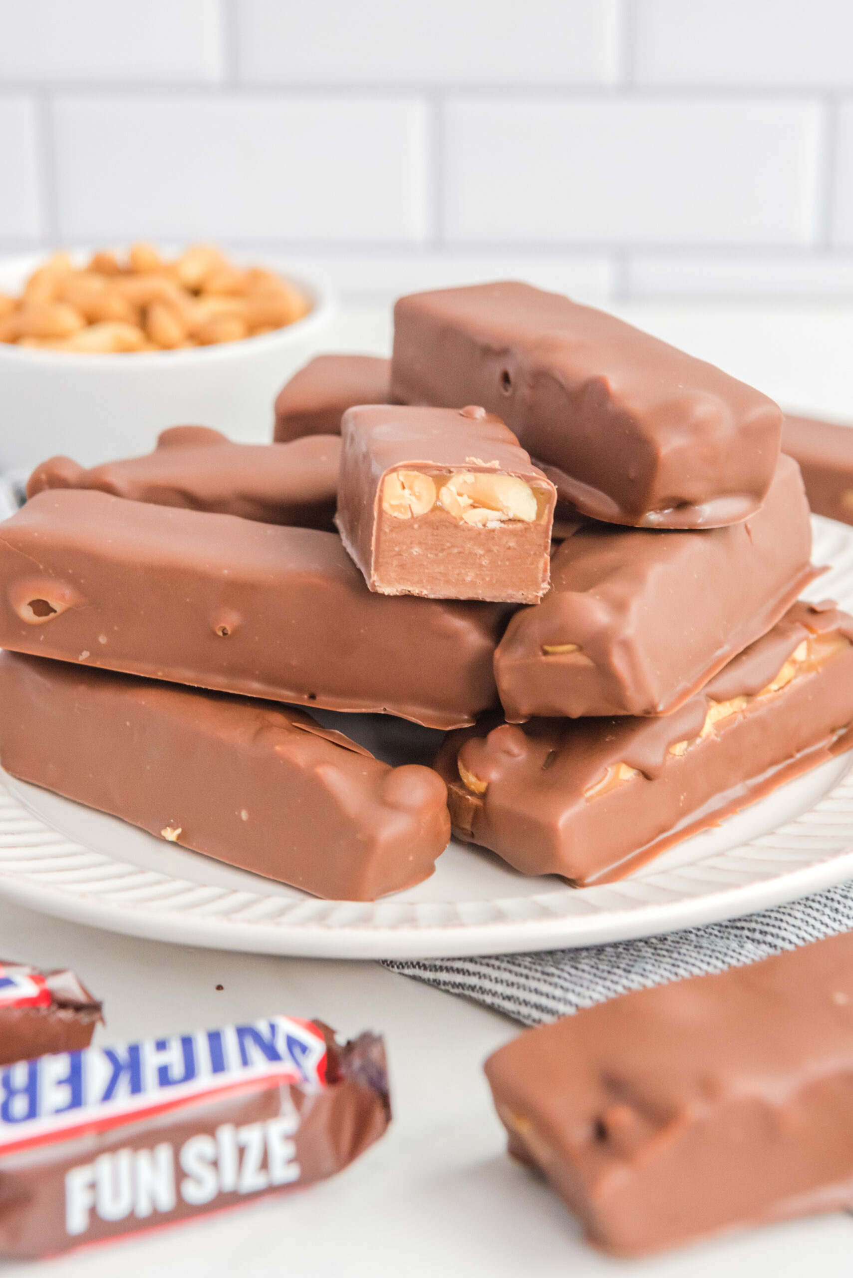 Front view of Homemade Snickers Bars stacked on a white plate with on bar cut in half.