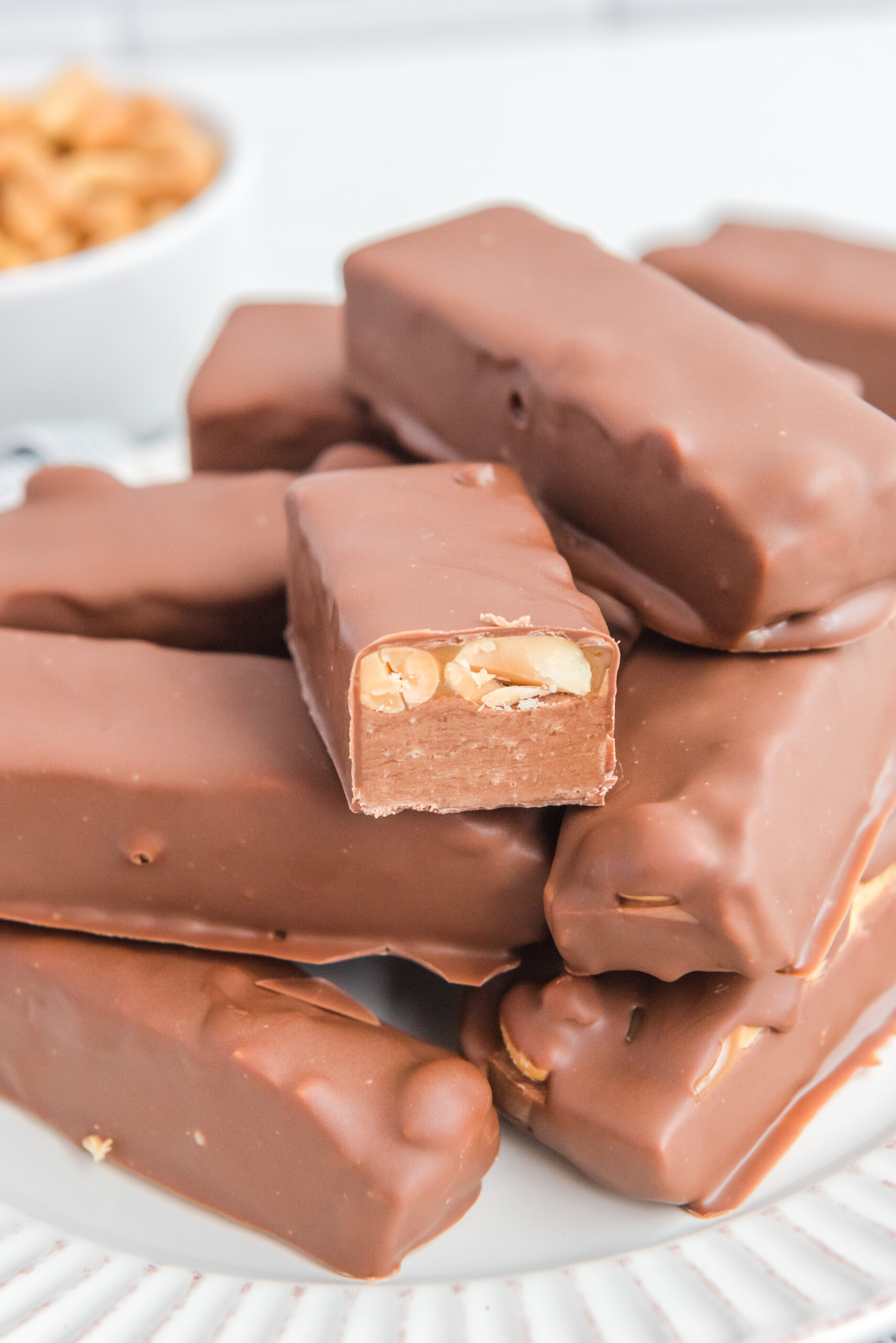 Homemade Snickers Candy Bars piled on a white serving plate with one cut open to show the inside