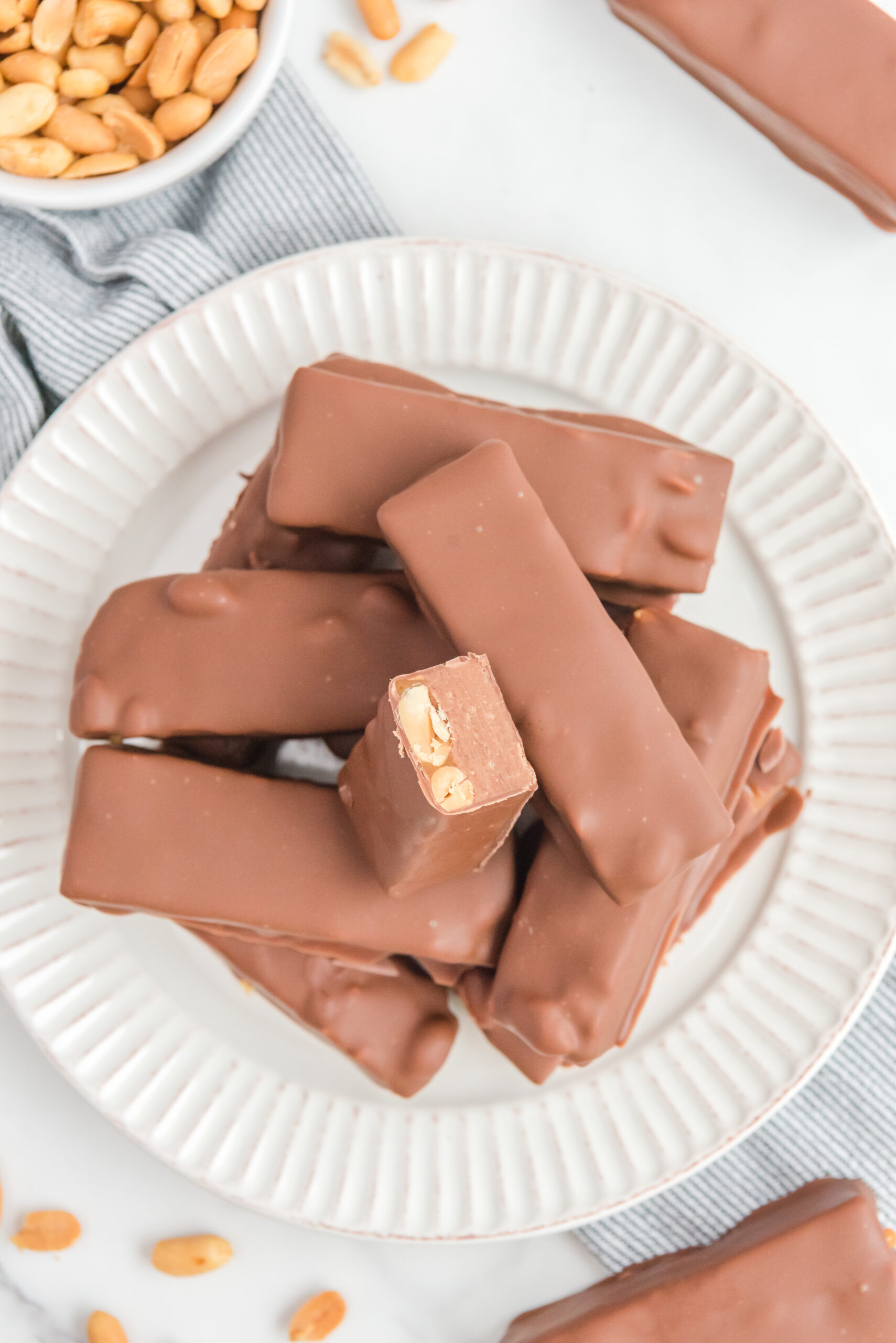 Overhead view of Homemade Snickers Bars stacked on a white plate with on bar cut in half.