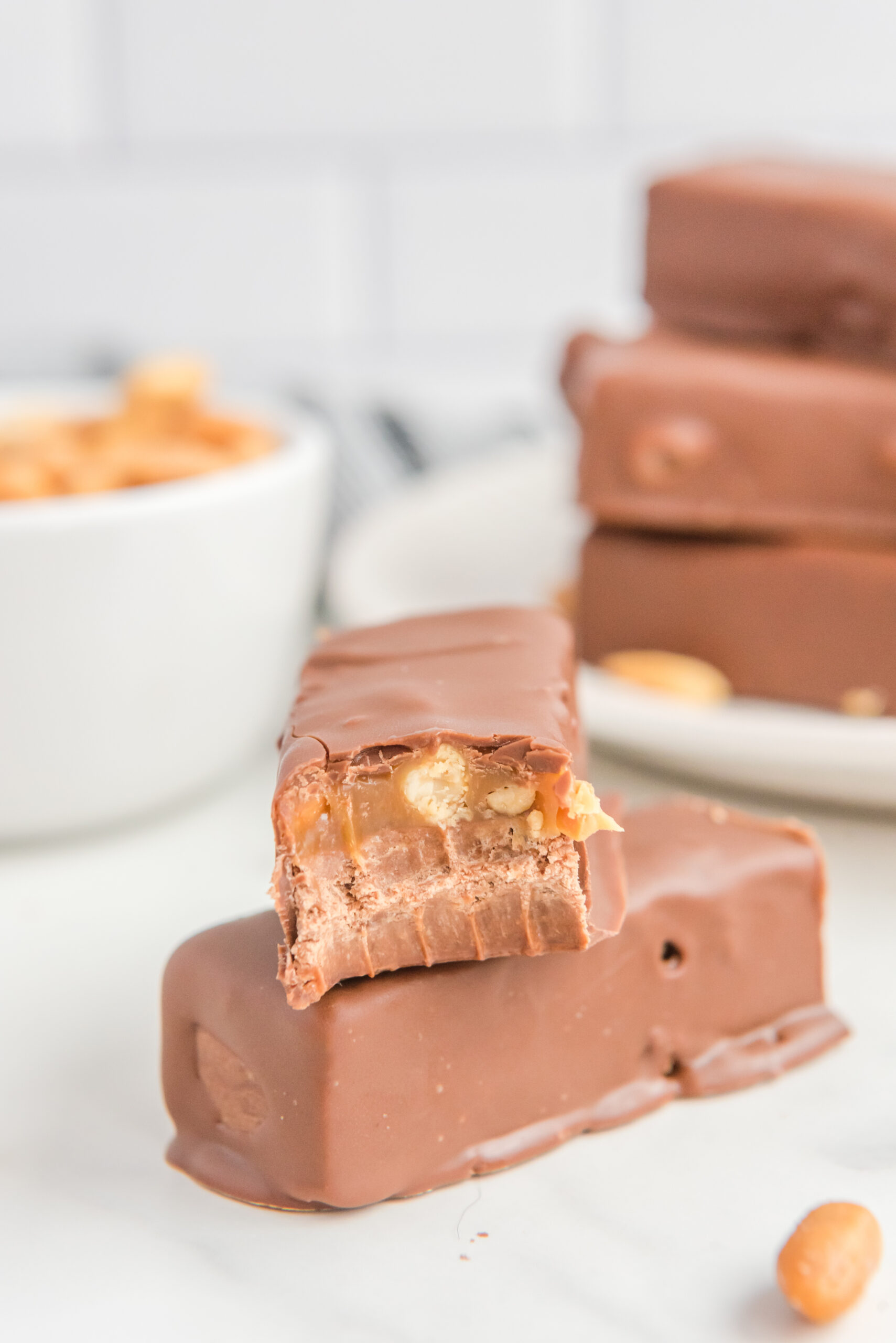 a couple Homemade Snickers Candy Bars on a table with a bite missing from one