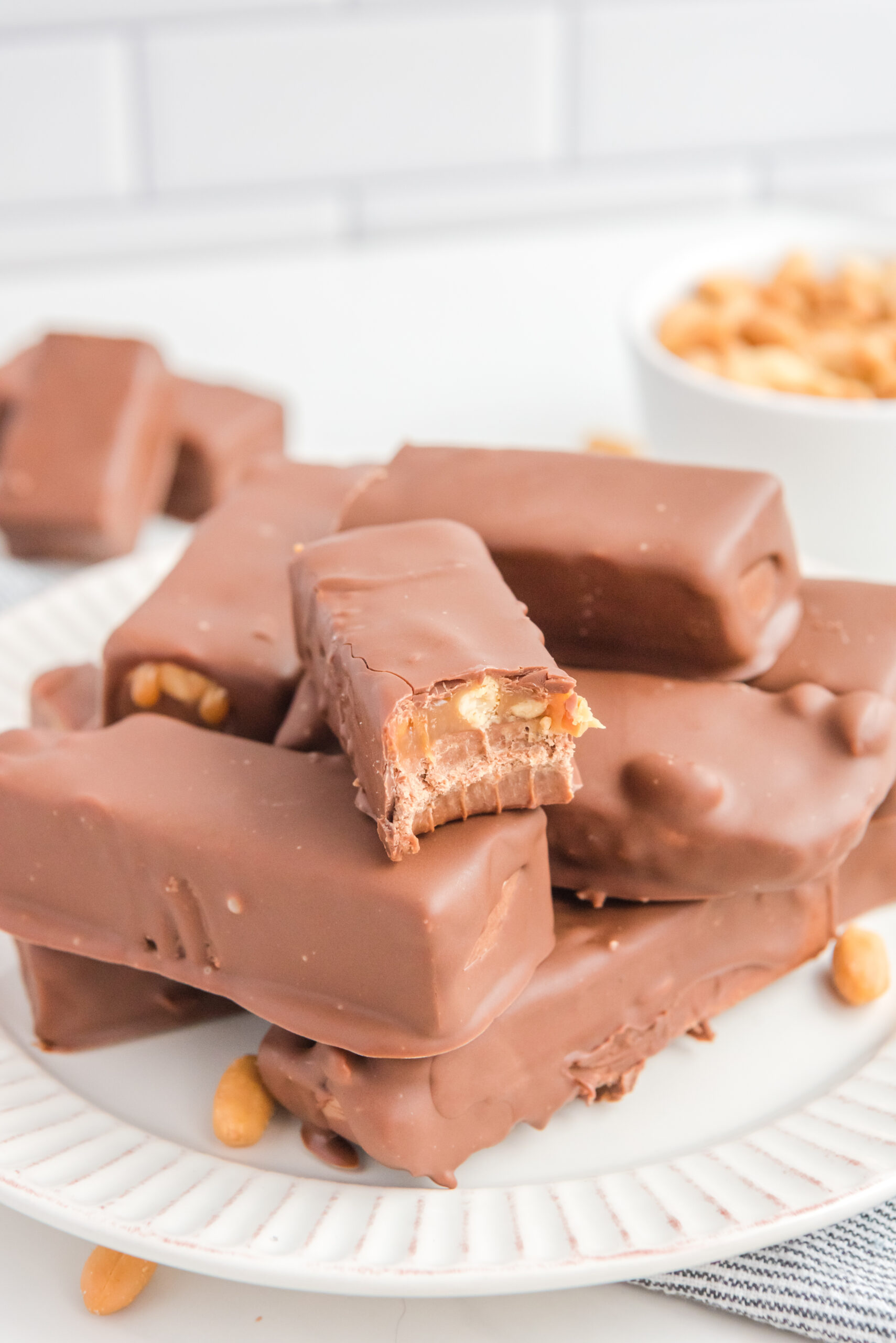 Homemade Snickers Candy Bars piled on a white serving plate with a bite missing from one