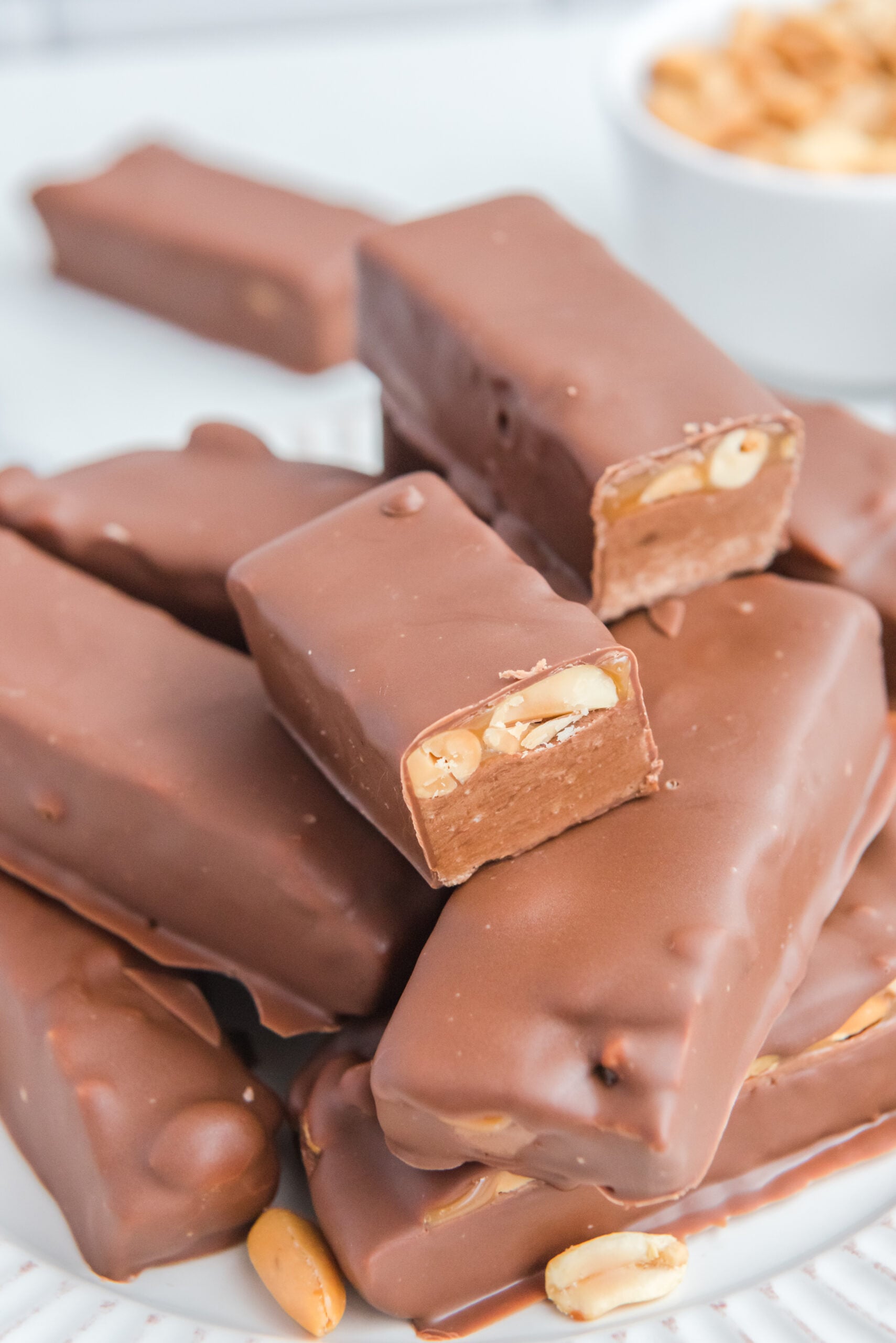 Homemade Snickers Candy Bars piled on a white serving plate with a bite missing from one