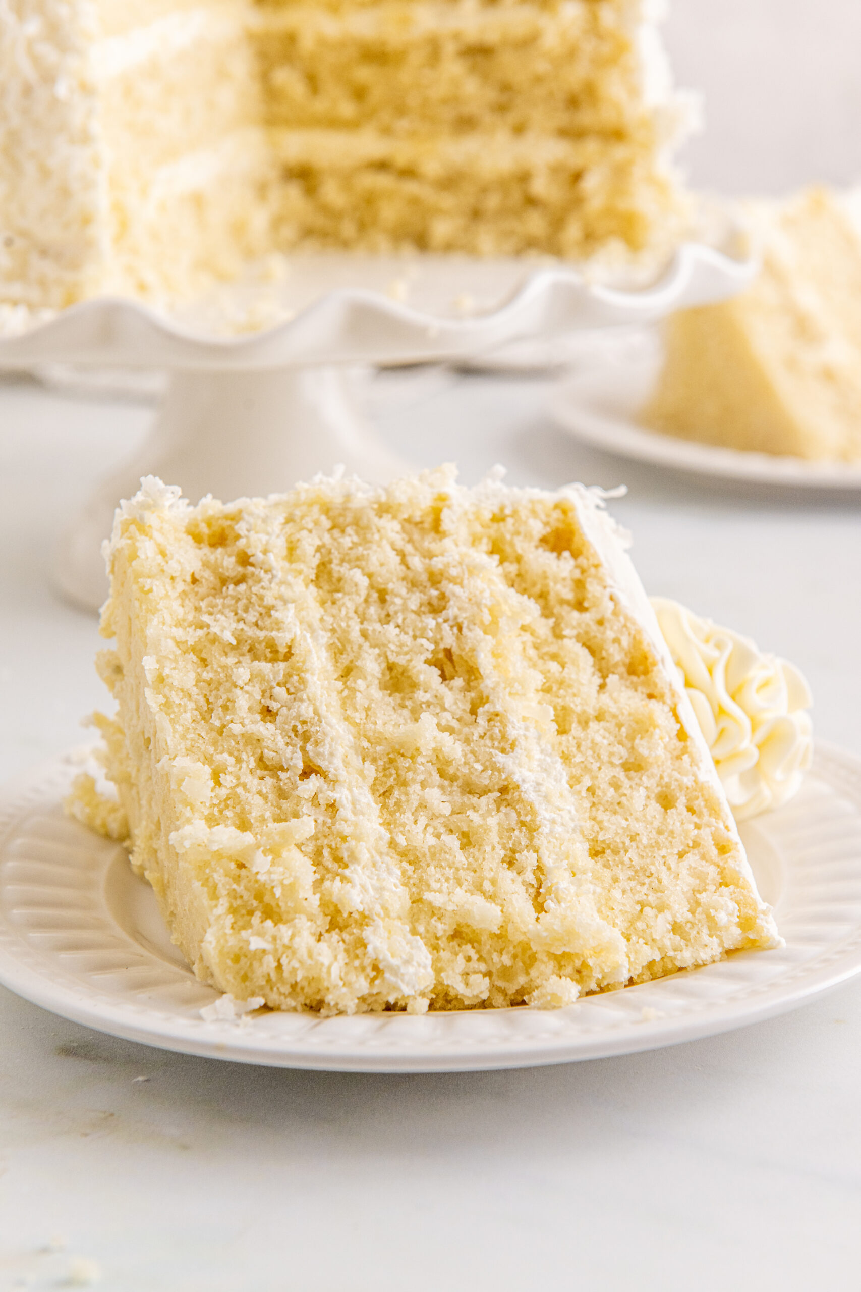 Front view of a slice of Coconut Layer Cake on a white plate.