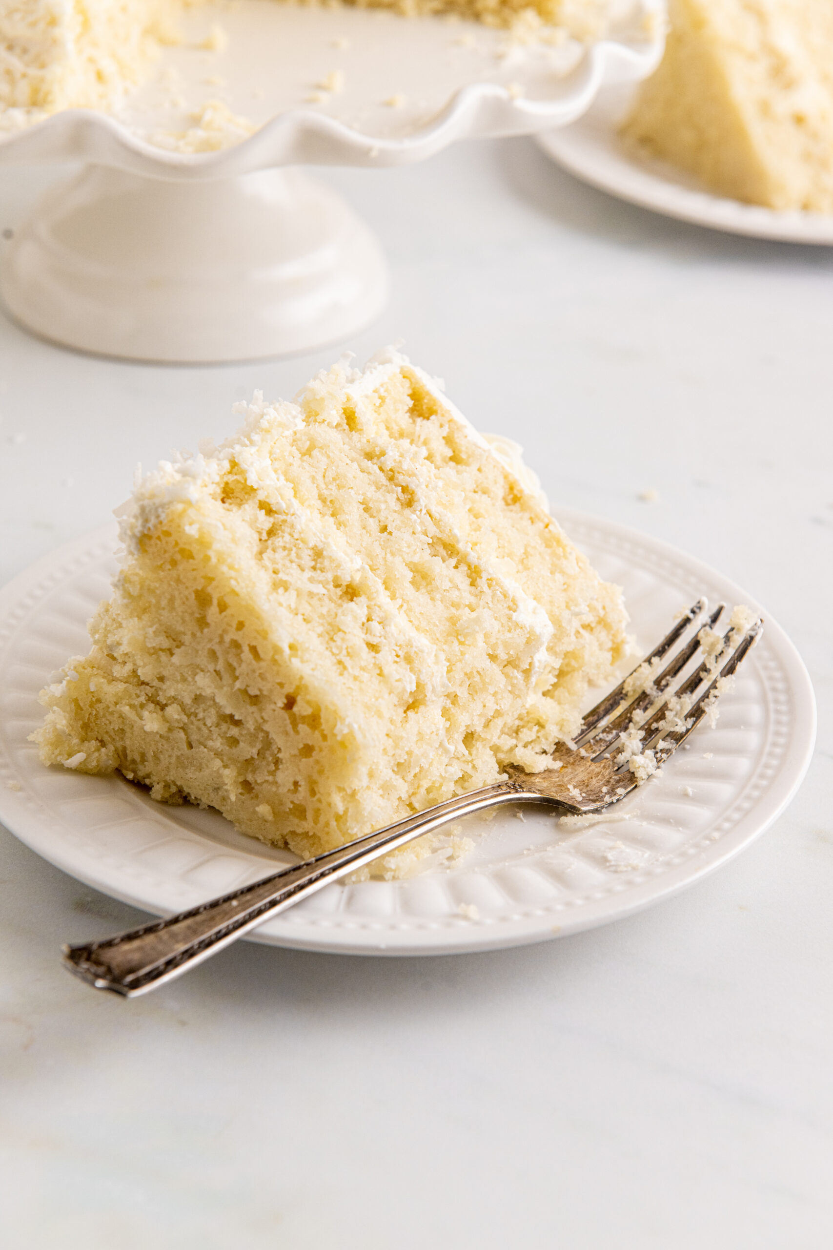 Front view of a slice of Coconut Layer Cake on a white plate with a bite removed.