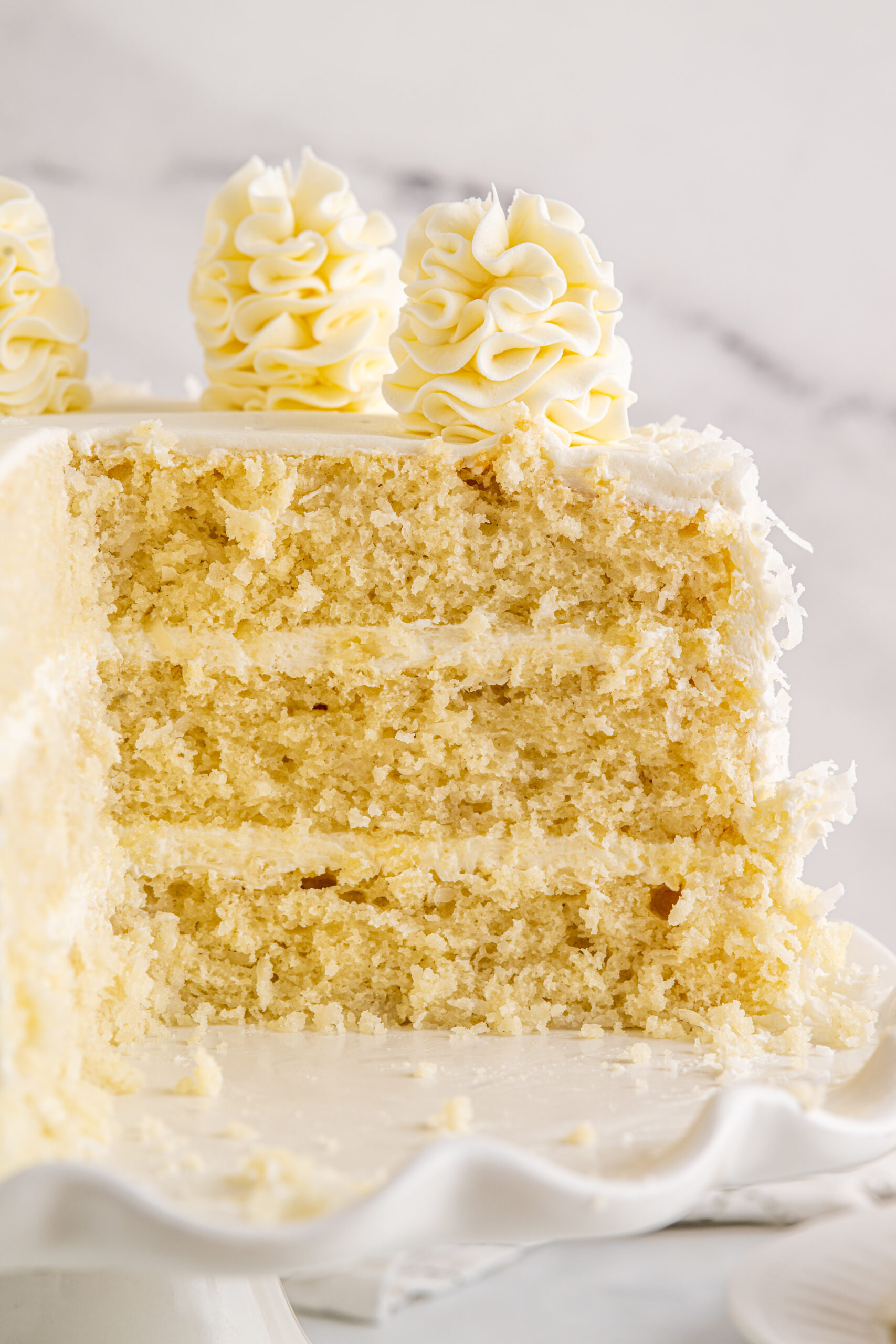 Close up view of Coconut Layer Cake on a white cake stand with two slices removed.