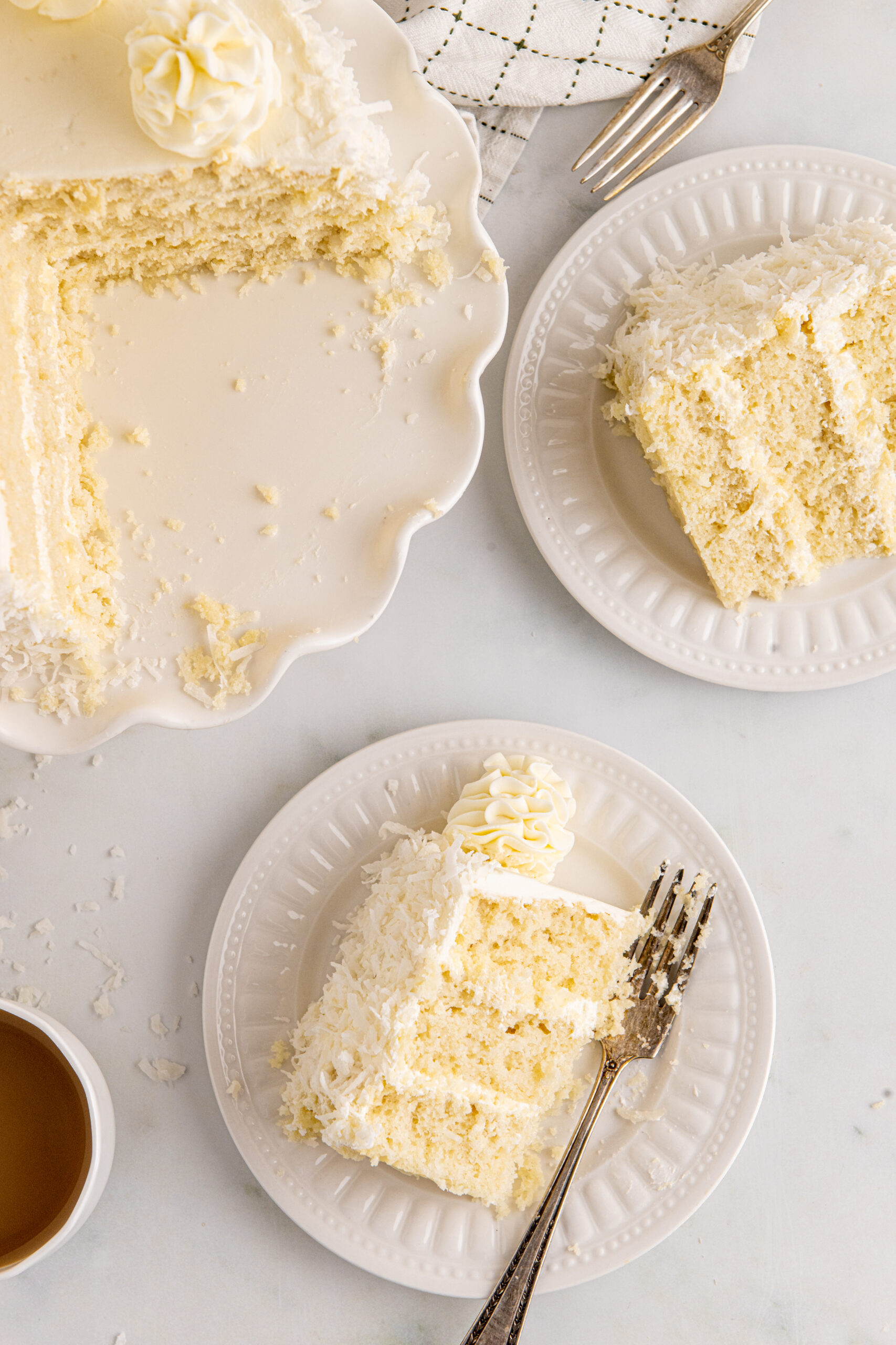 Overhead view of a slice of Coconut Layer Cake on a white plate with a bite removed by a silver fork.