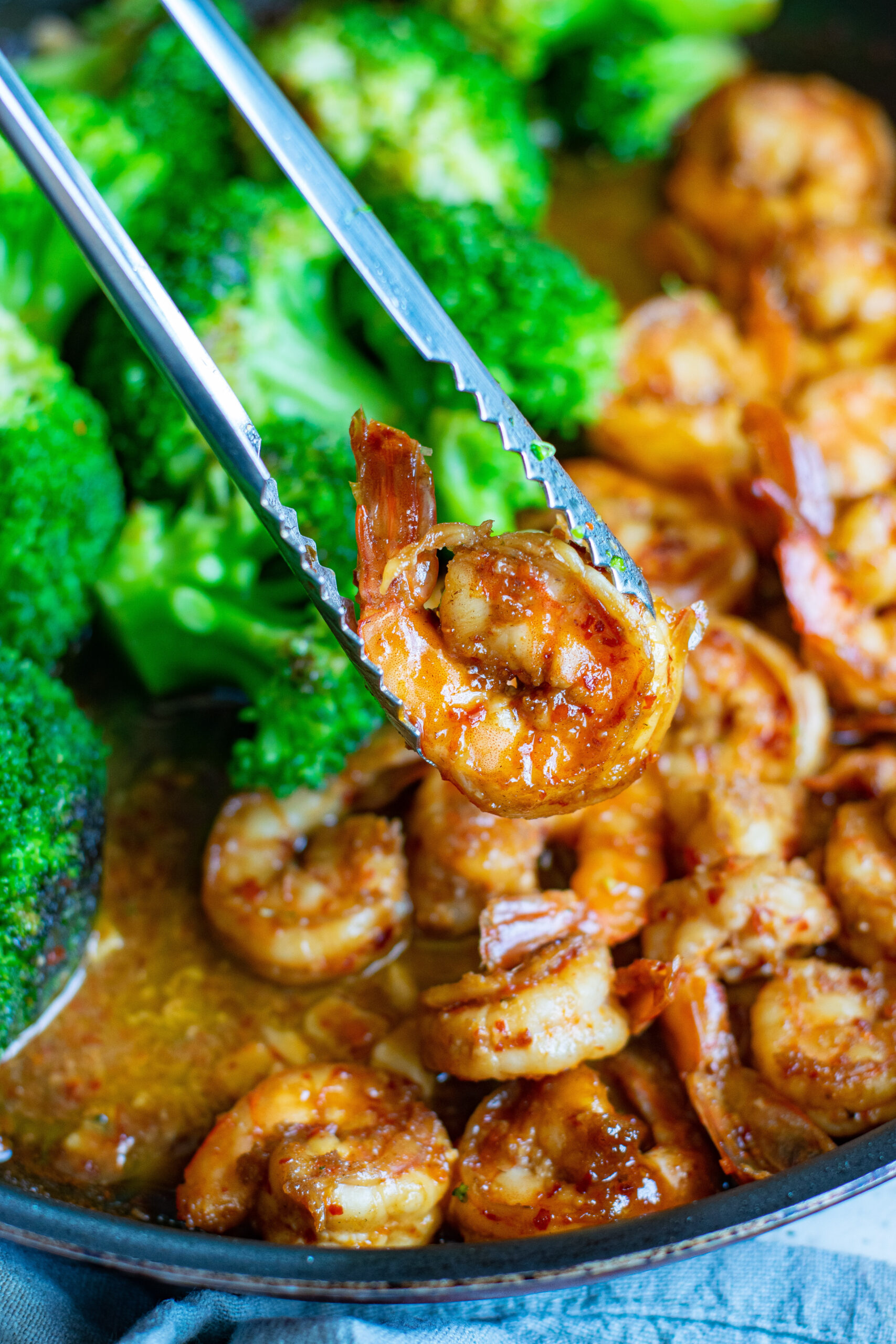 A pair of silver tongs removing a piece of shrimp from the skillet.