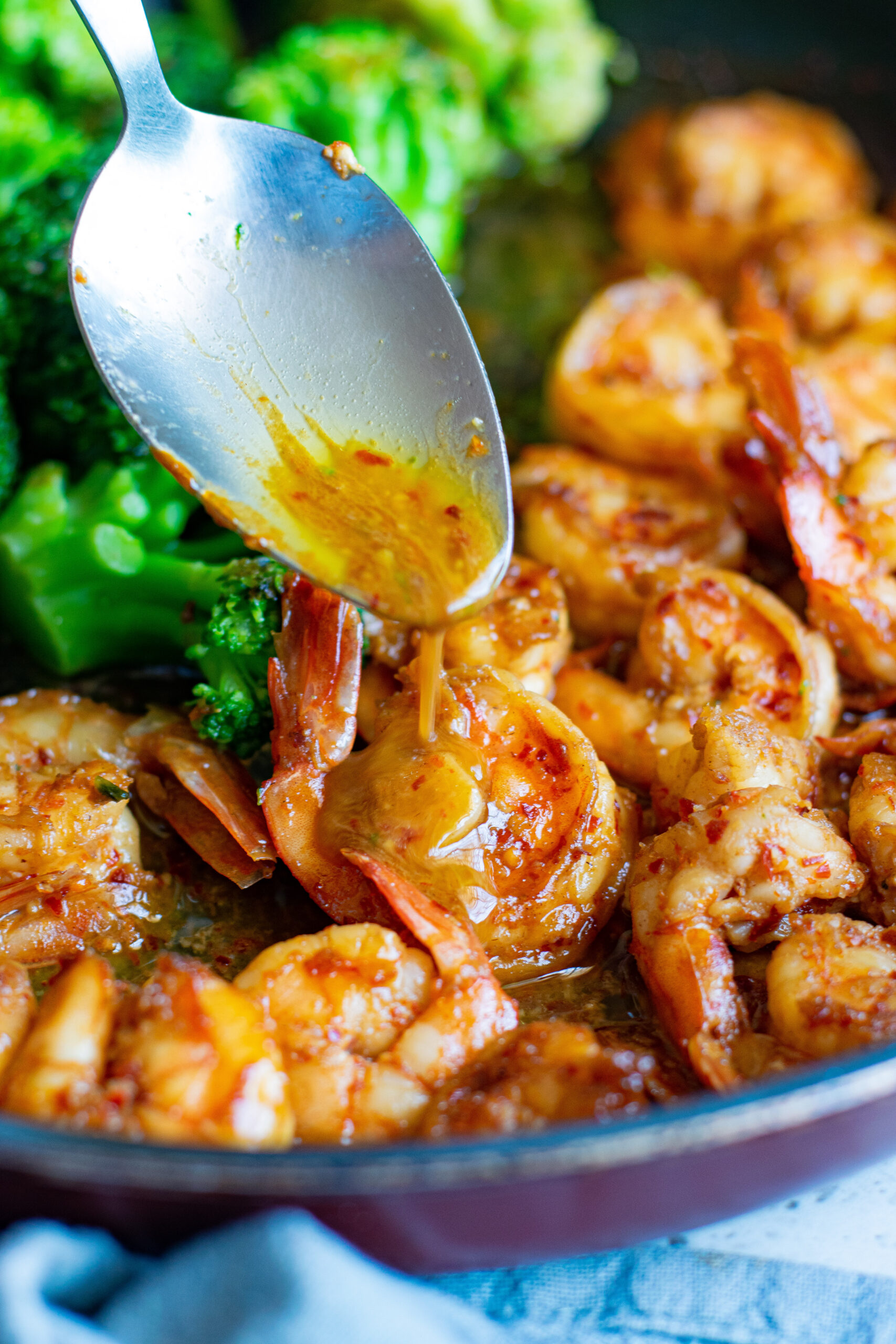 A silver spoon spooning sauce over the shrimp.