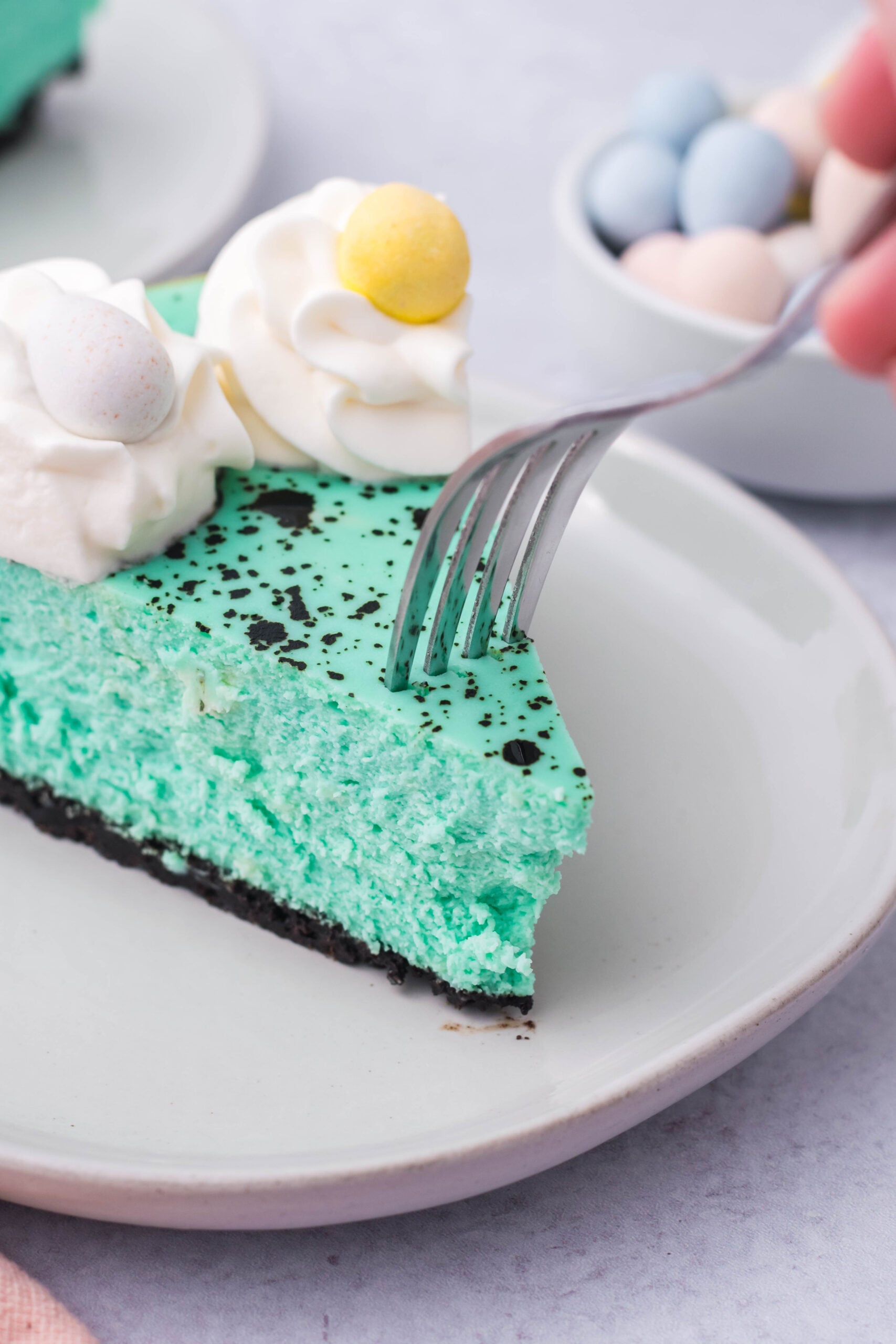 Close up view of a bite being removed from a slice of Speckled Egg Cheesecake with a silver fork.