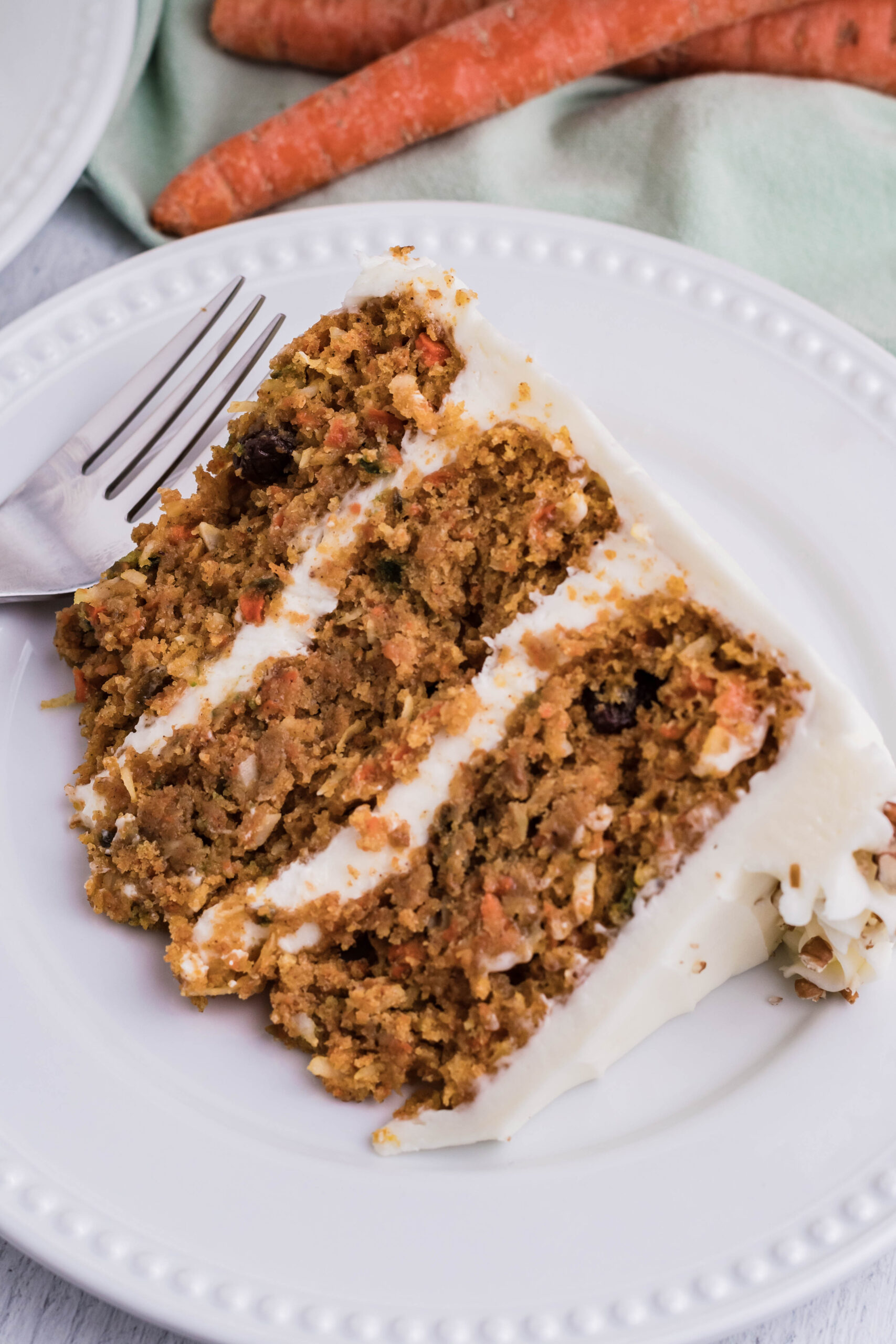Close up view of a slice of Carrot Cake served on a white plate.