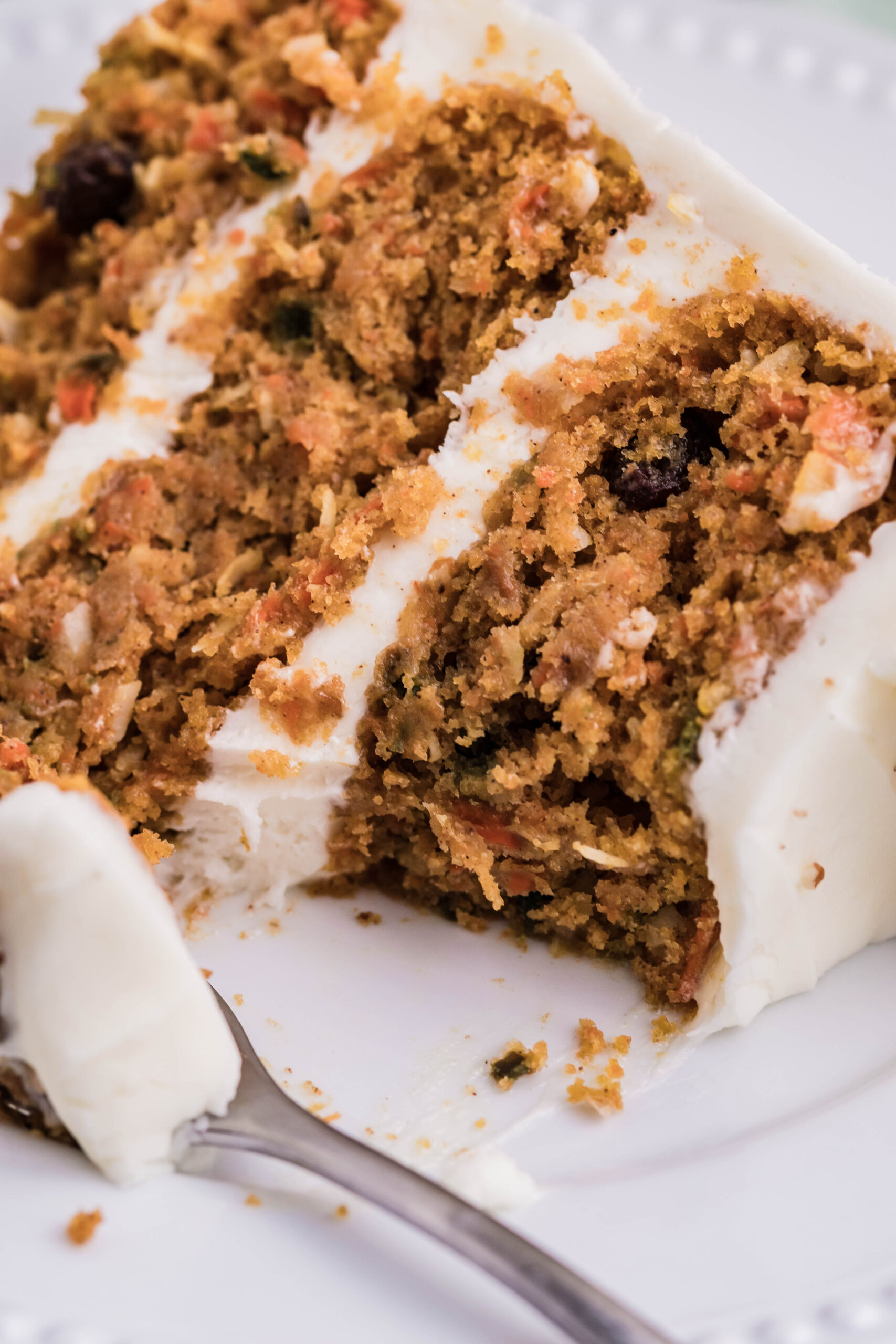 Close up view of a slice of Carrot Cake served on a white plate with a bite removed.