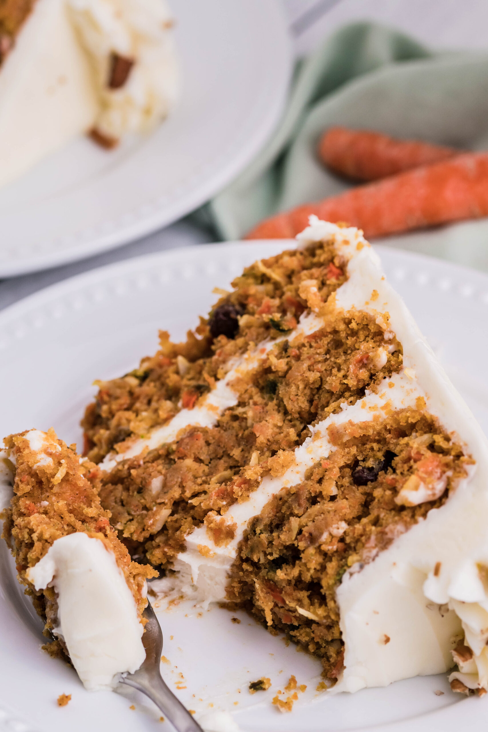 Close up view of a slice of Carrot Cake served on a white plate with a bite removed.