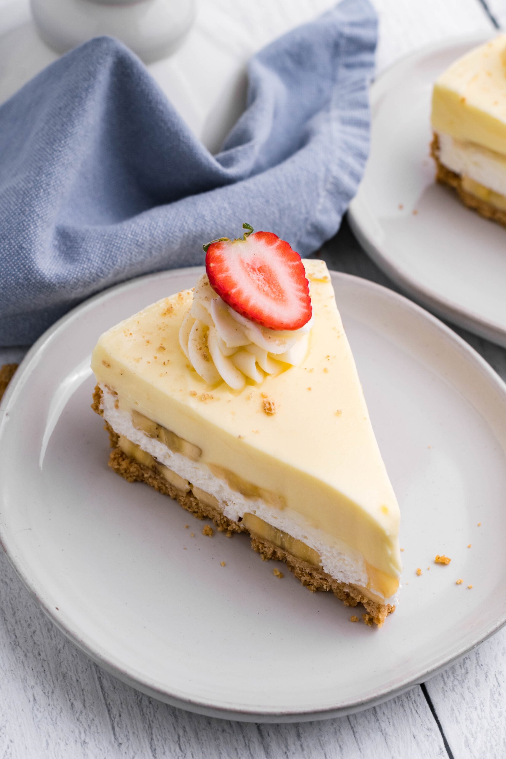 Close up view of a slice of Banana Cream Cheesecake on a white plate.