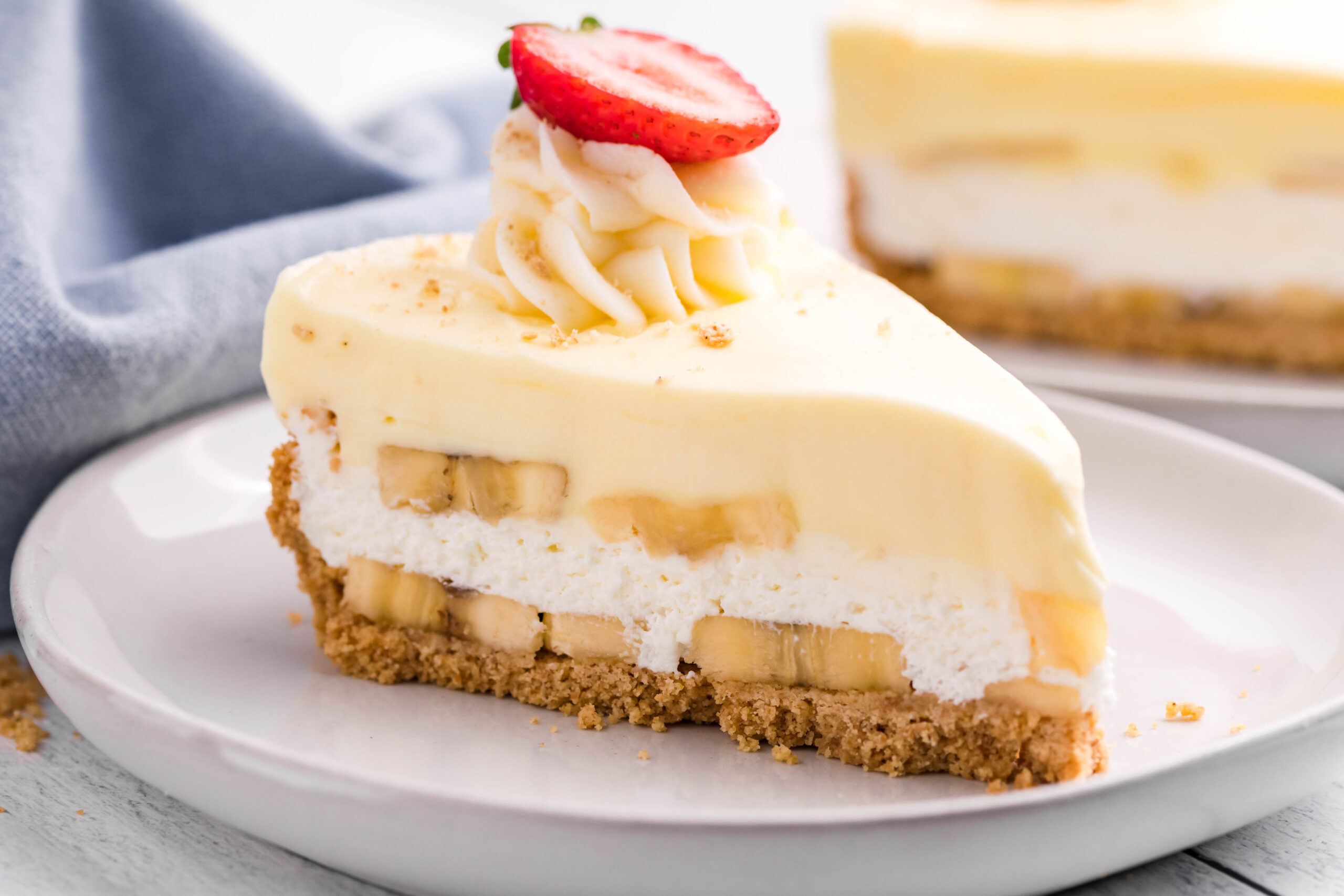 Side view of a slice of Banana Cream Cheesecake on a white plate.
