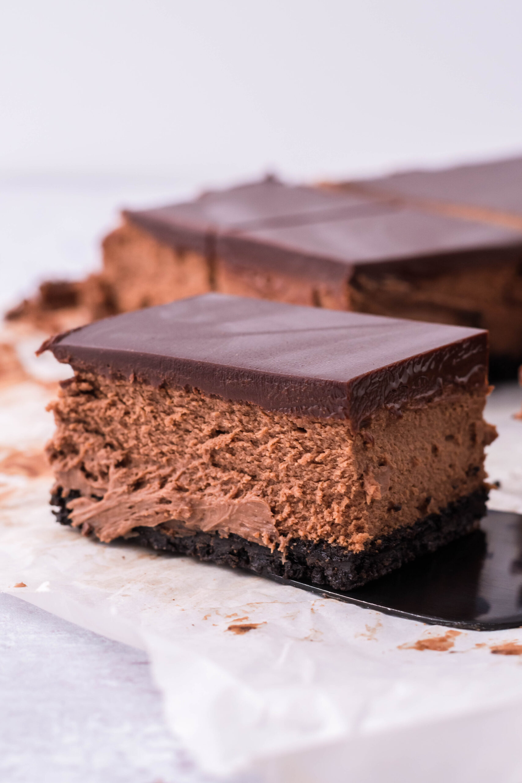 A bar of chocolate cheesecake being removed with a black spatula. 