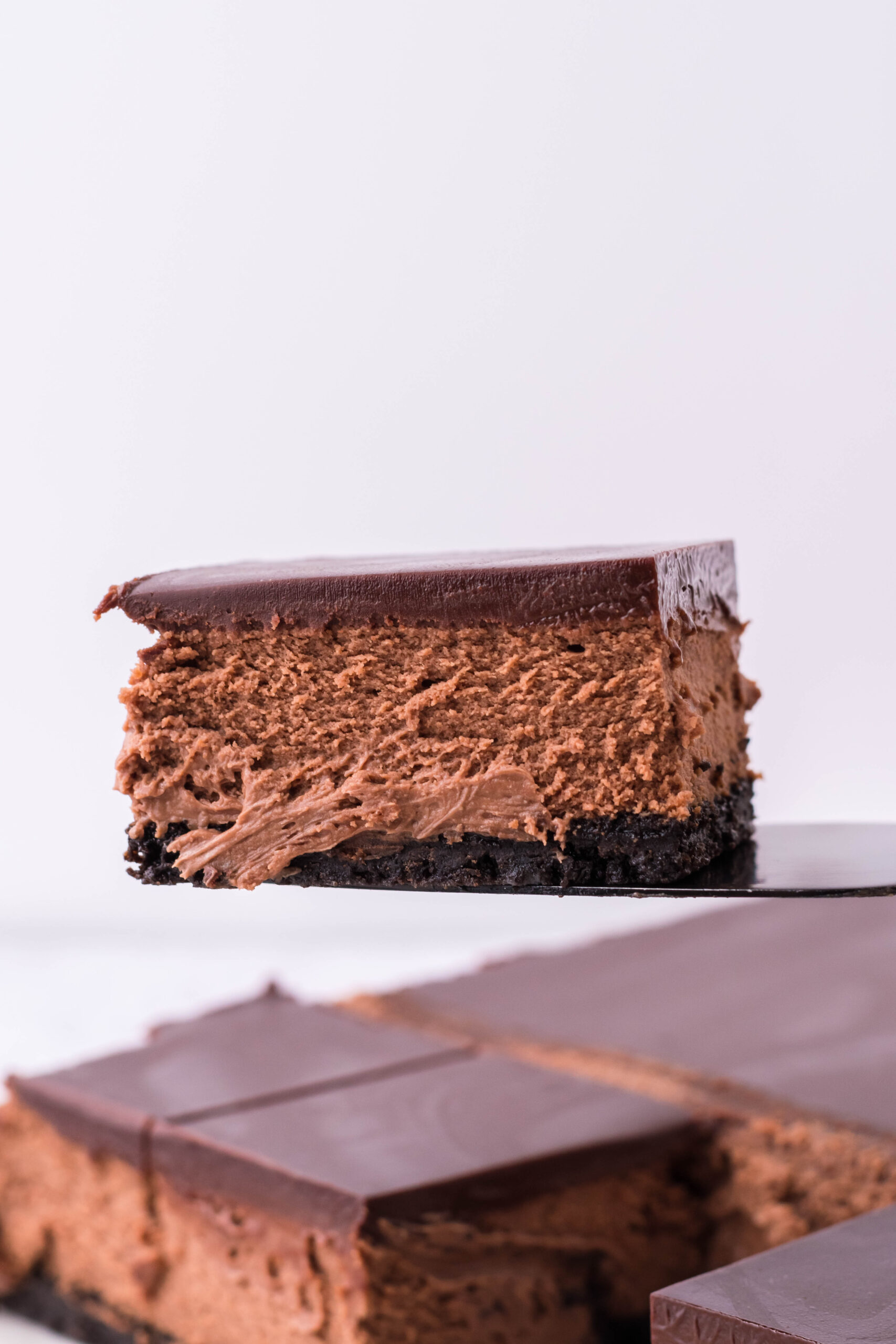 A black spatula picking up a bar of chocolate cheesecake. 