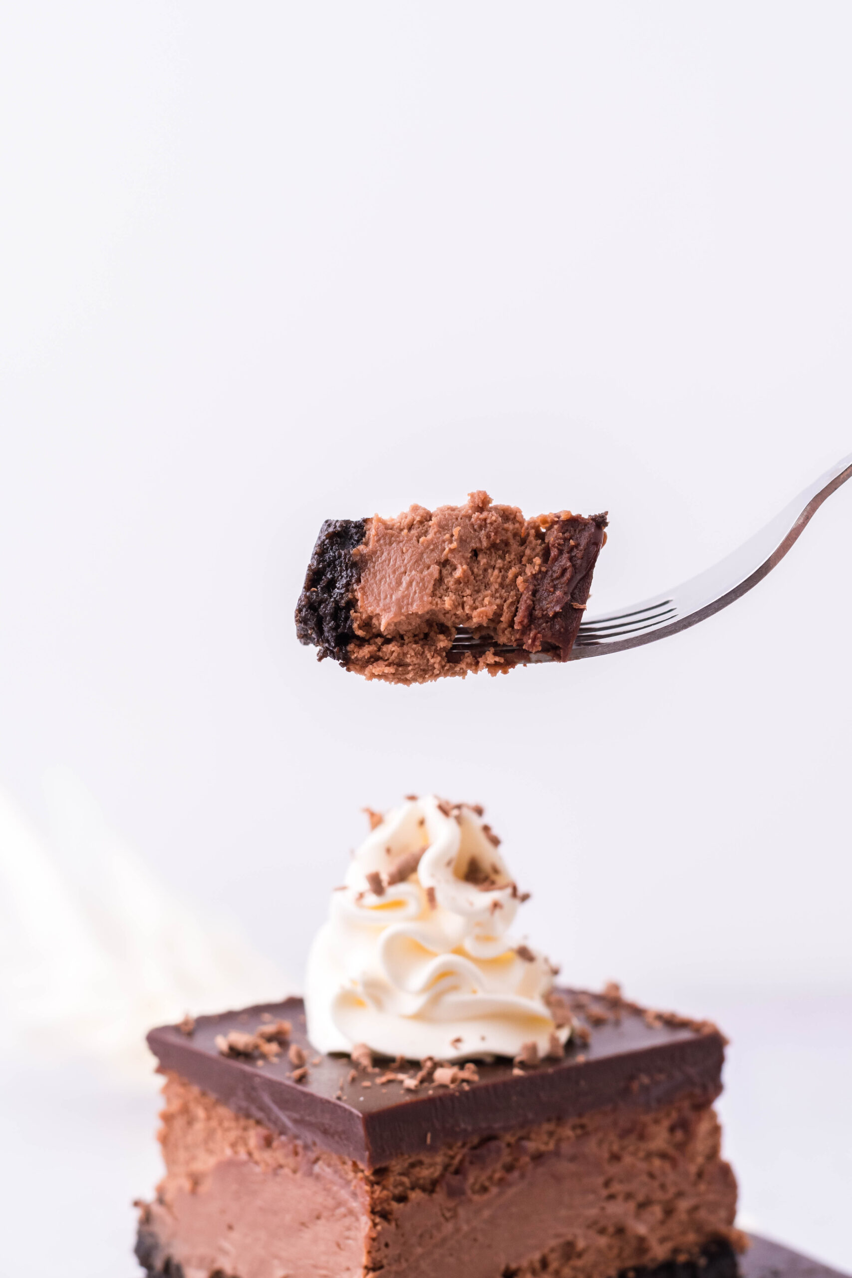 A bite of cheesecake on a silver fork with the cheesecake bars in the background. 