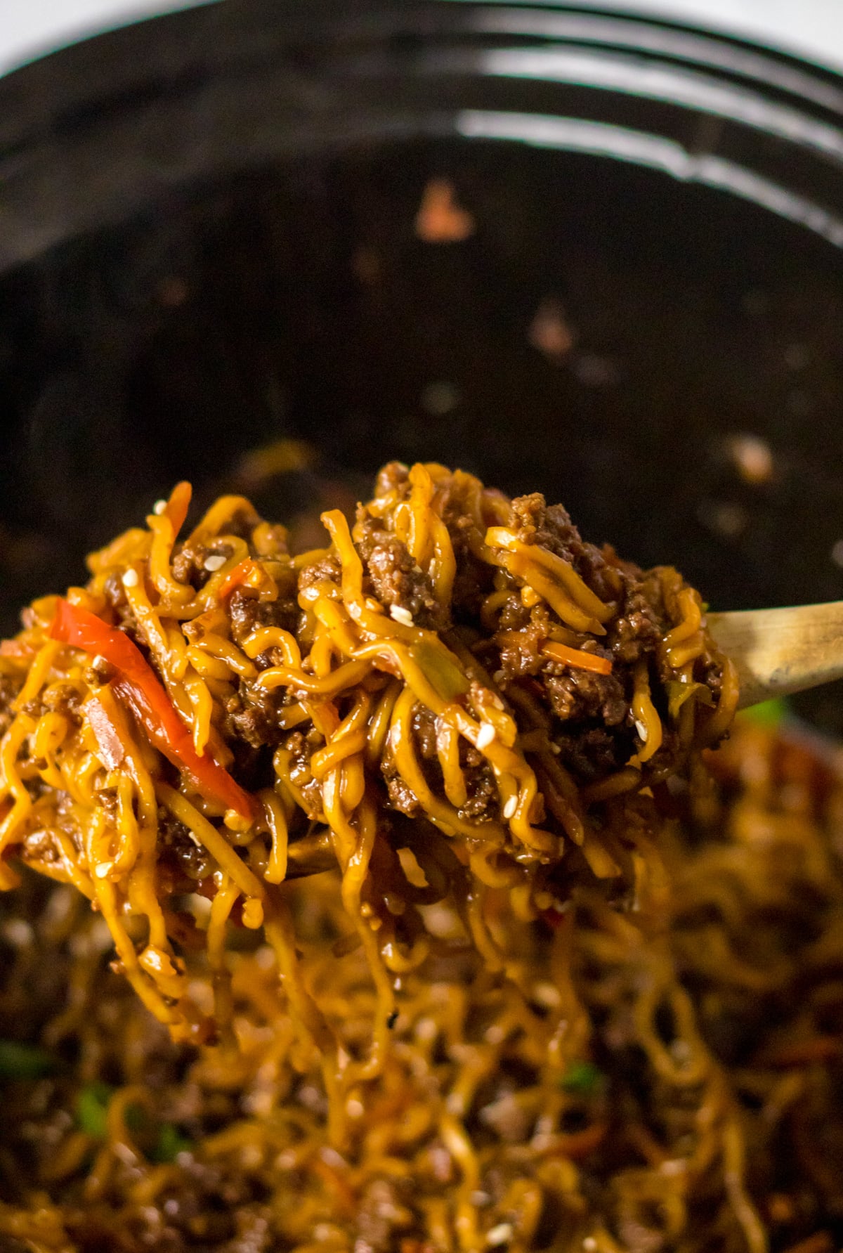 Close up view of Slow Cooker Beef Ramen in a crock pot with a wooden spoon removing a serving.