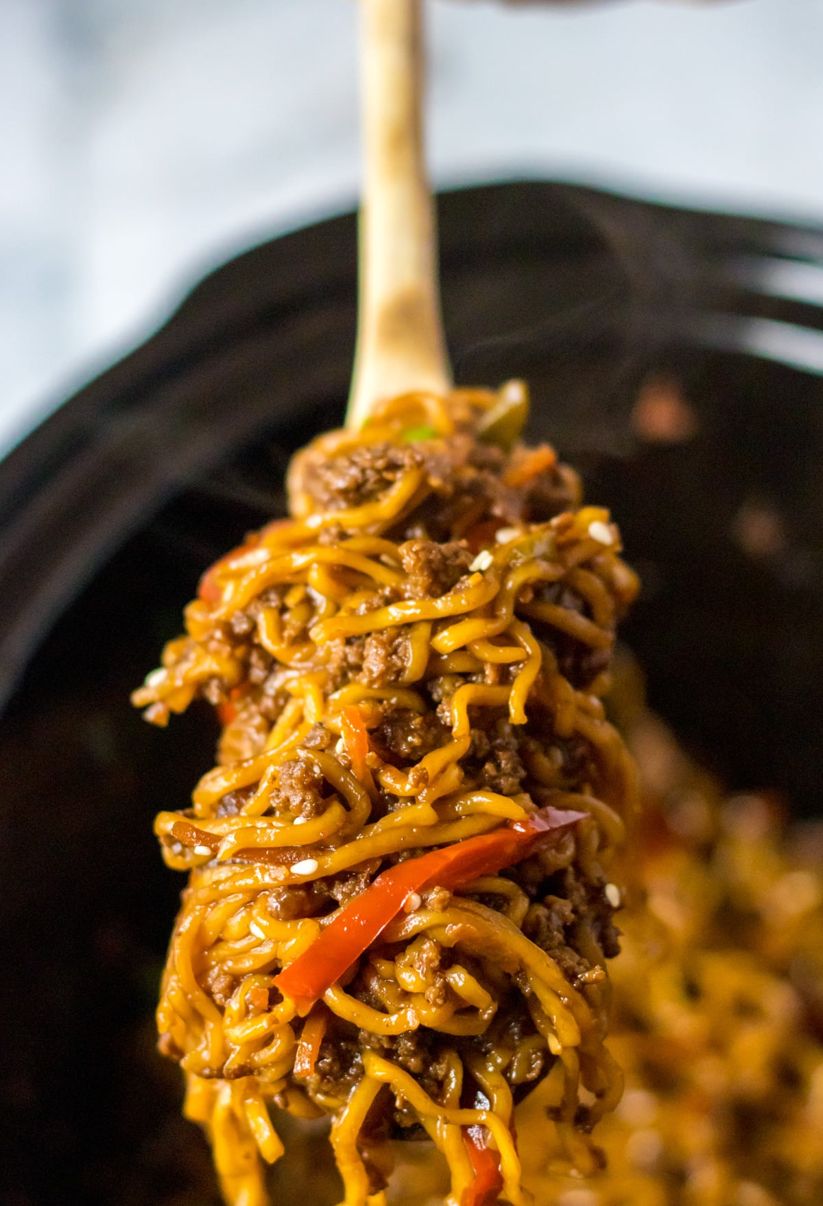 Close up view of Slow Cooker Beef Ramen in a crock pot with a wooden spoon removing a serving.