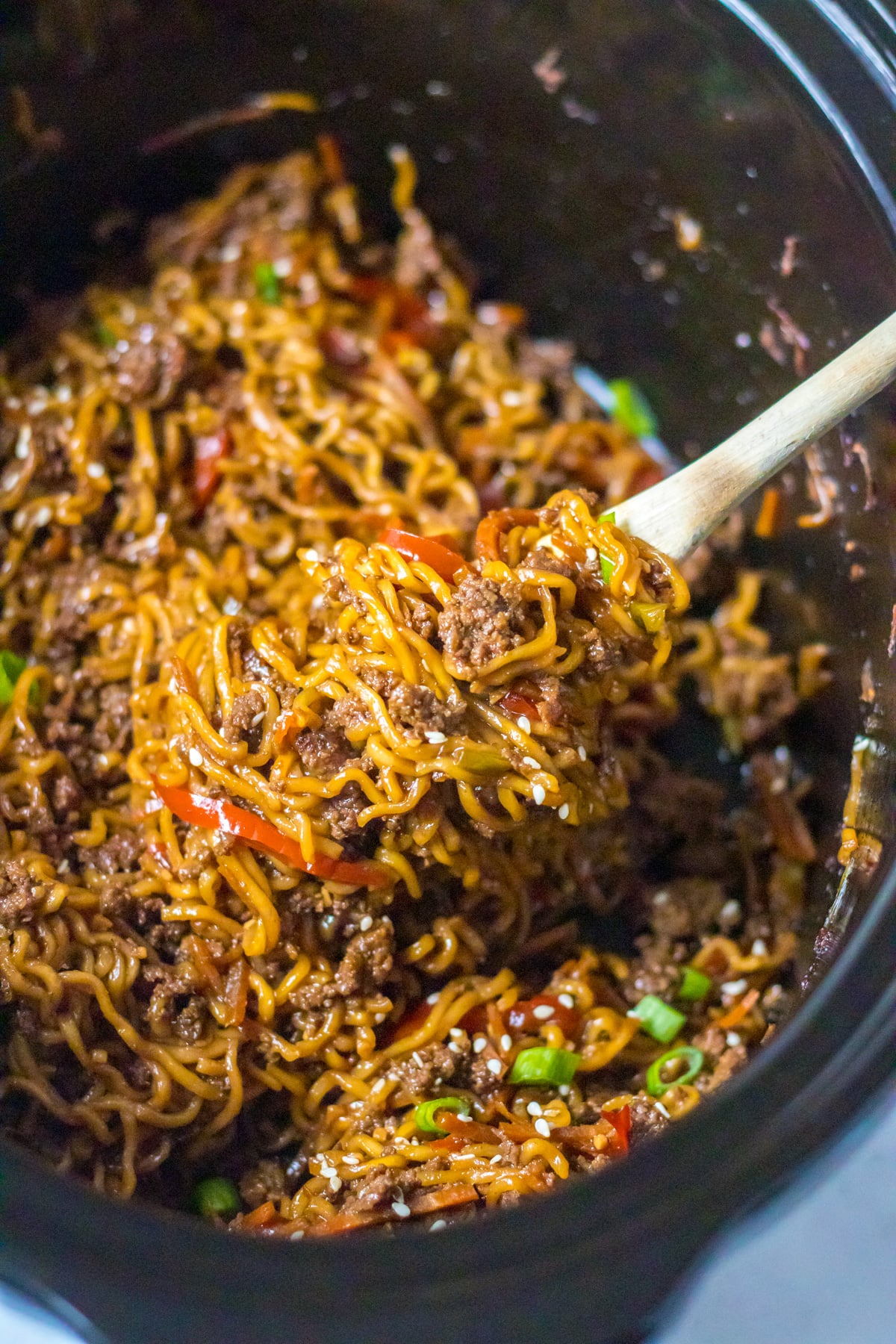 View of Slow Cooker Beef Ramen in a crock pot with a wooden spoon removing a serving.
