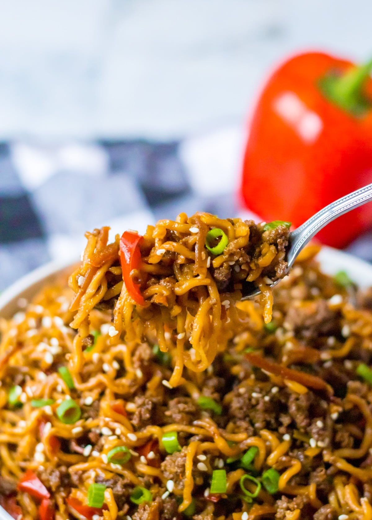 Front view of Slow Cooker Beef Ramen in a white bowl with a silver fork removing a bite.