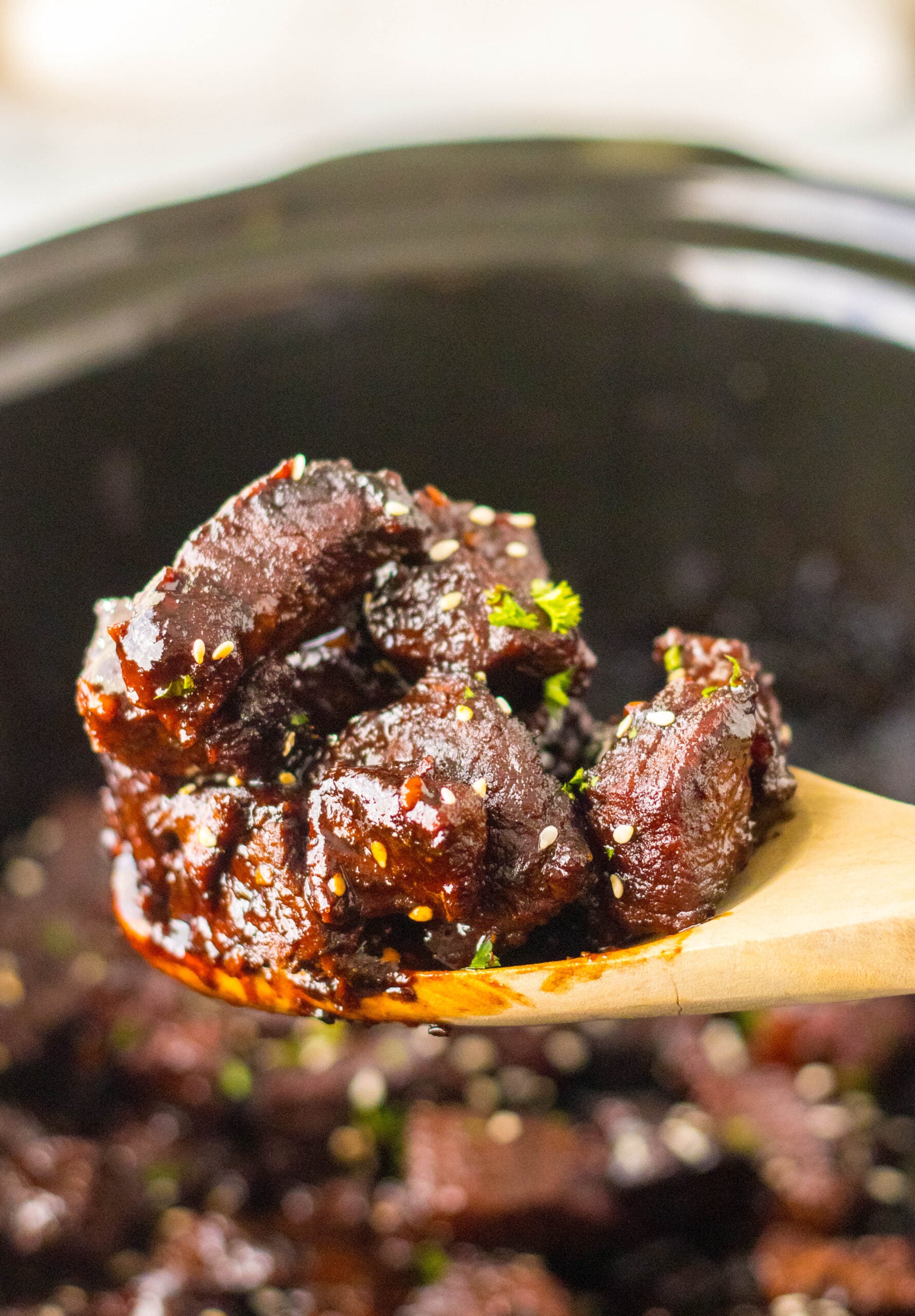 Close up view of a wooden spoon with a spoonful of Slow Cooker Honey Garlic Steak Bites.